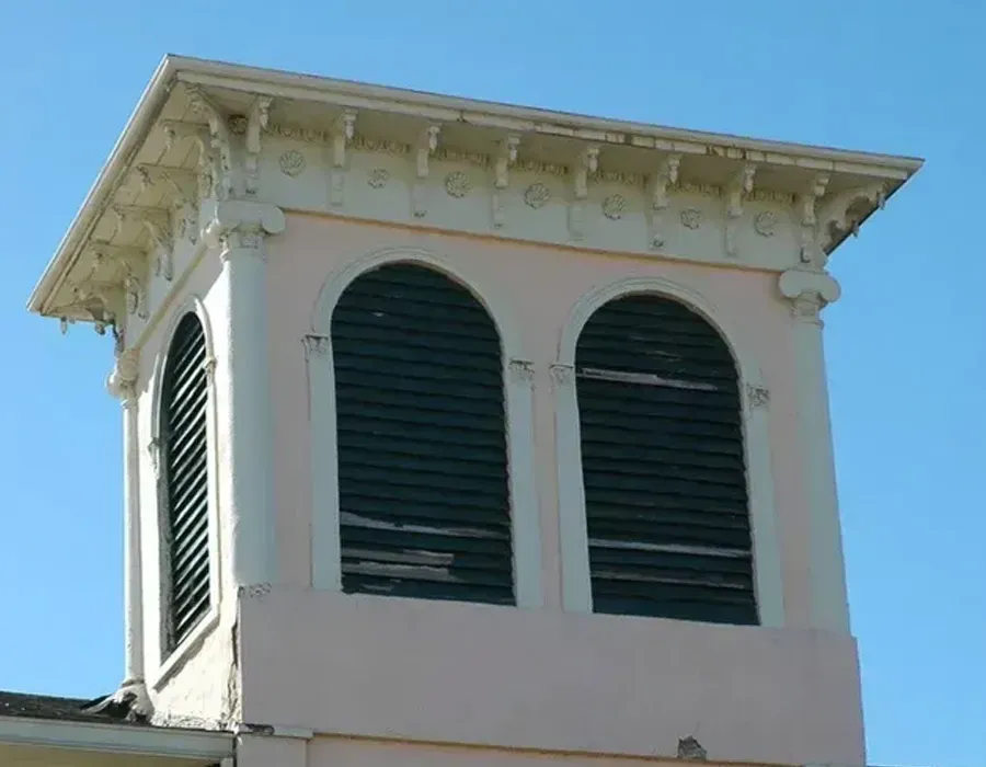 White building cupola with two arched louvered windows and ornate roof trim against blue sky