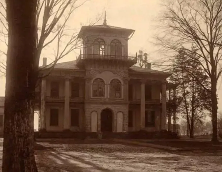 Sepia-toned photo of a large historic mansion with columns and a cupola, framed by bare trees