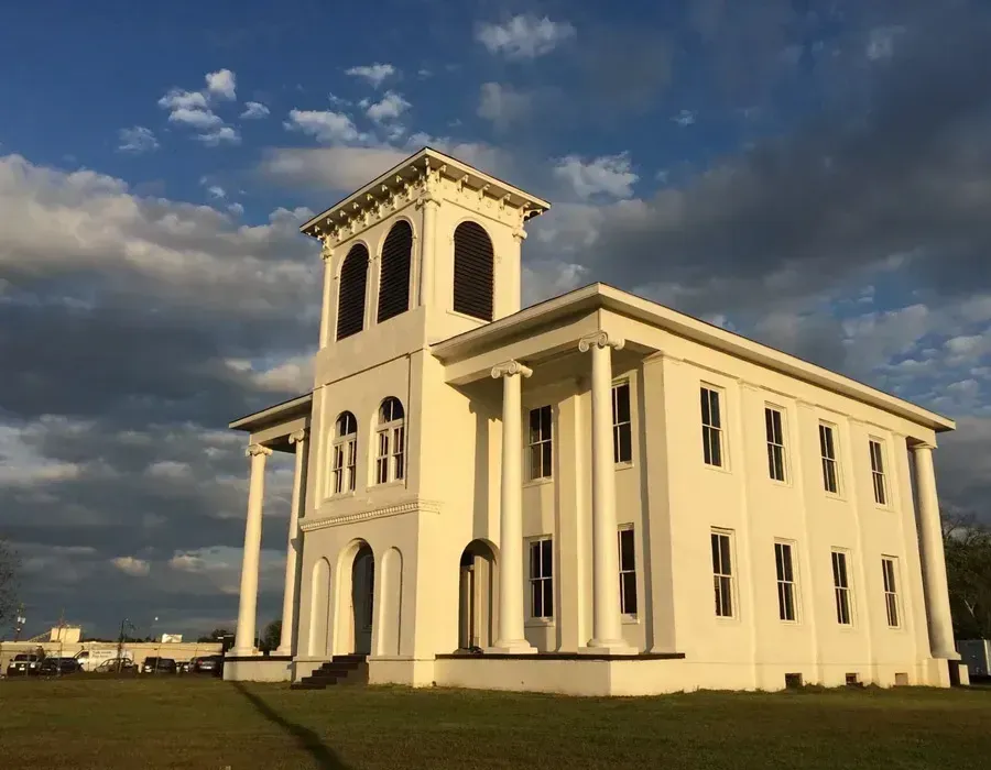 White historic building with tower under a cloudy sky, standing on a grassy field