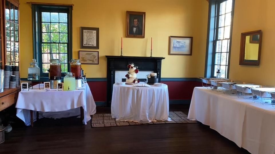 A catering setup with drink dispensers and buffet chafing dishes on white-clothed tables in a room with yellow walls.