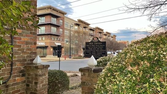 A brick entrance with a historical marker standing before a multi-story, modern brick apartment complex on a sunny day.