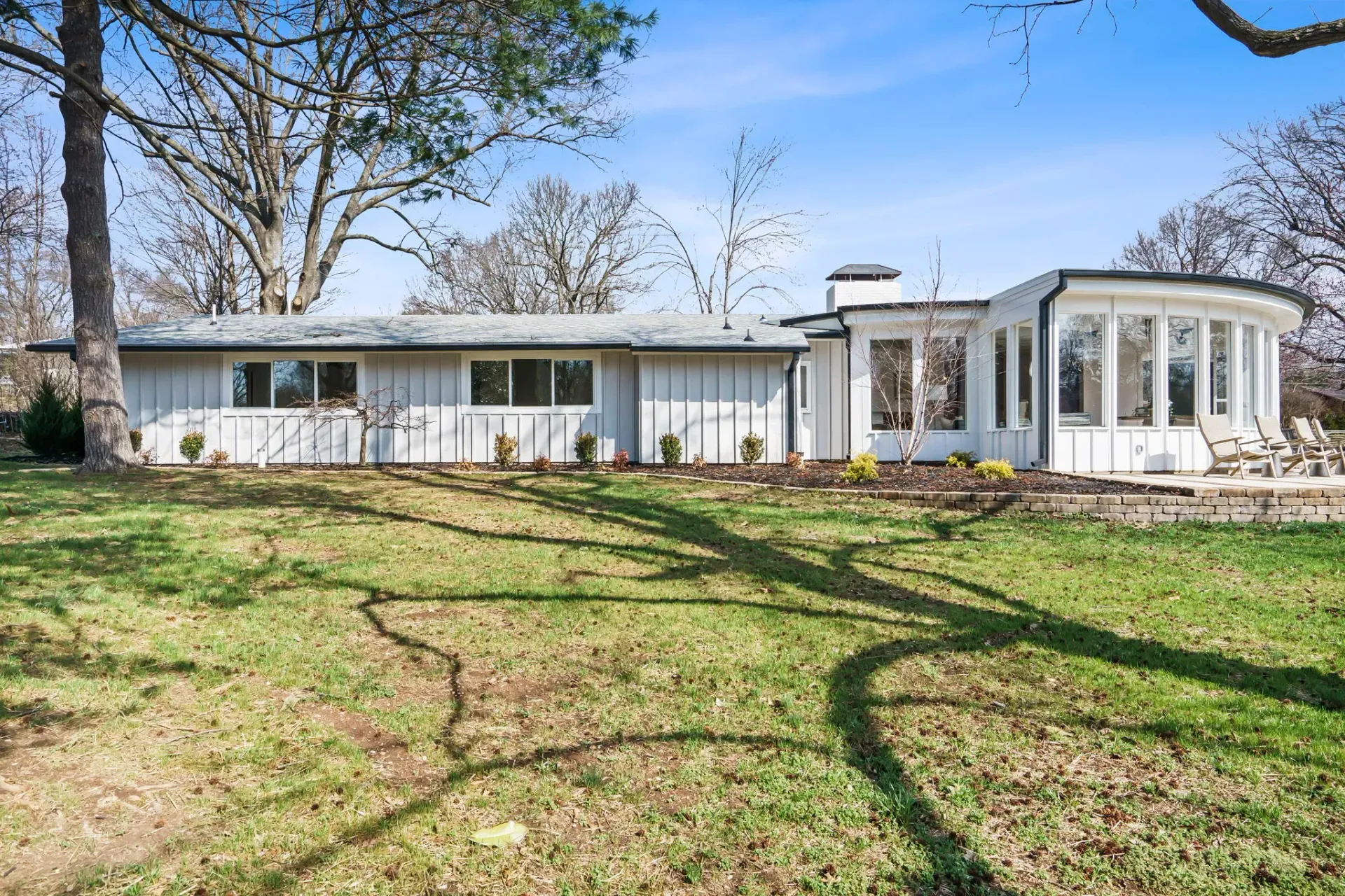 Single-story white house with a front lawn and large windows under leafless trees