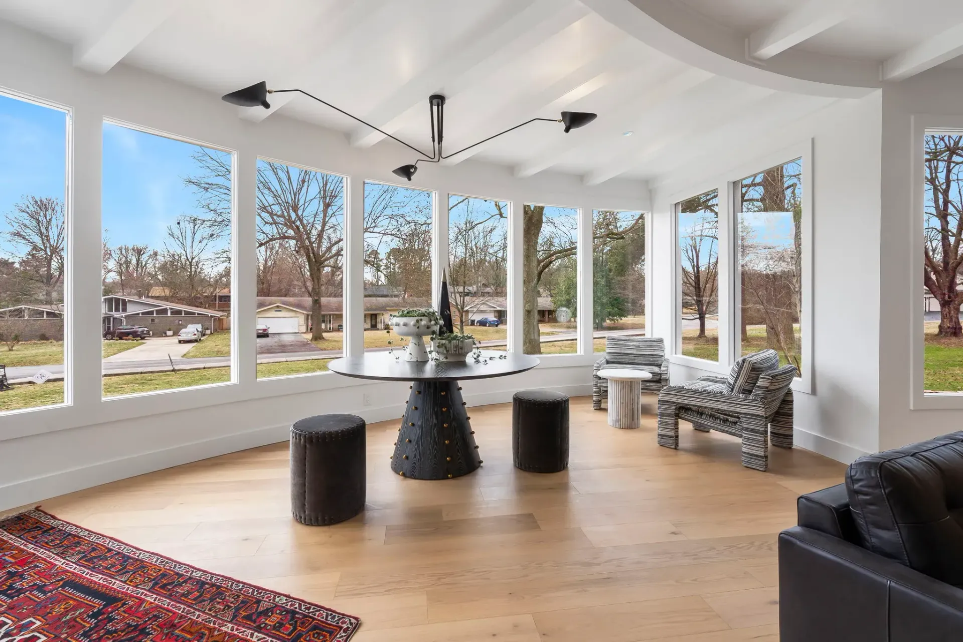 Bright modern living room with curved windows, wood floor, black furniture, and a snowy outdoor view