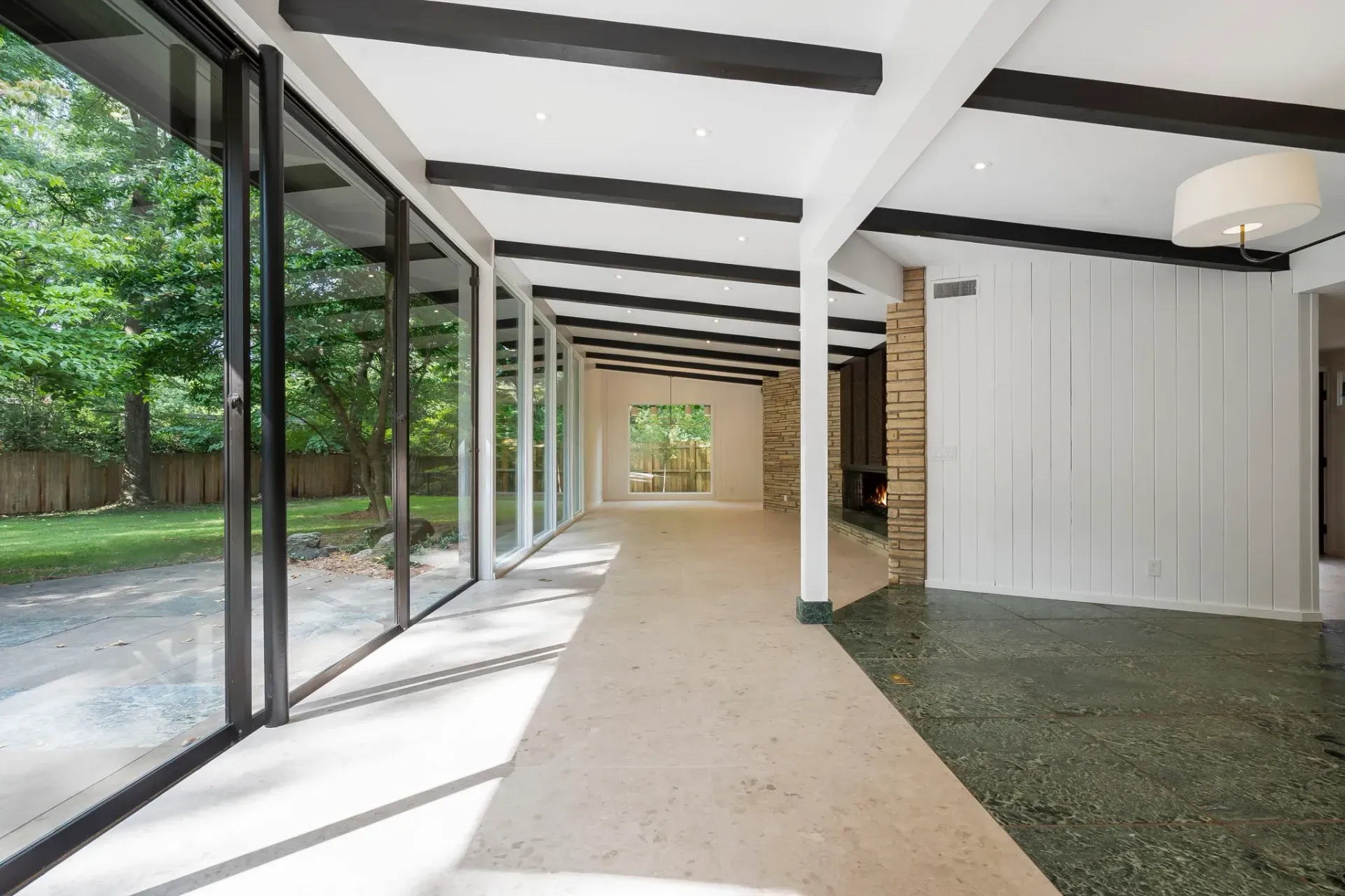 Bright covered walkway with glass walls, white beams, and gravel courtyard beside trees