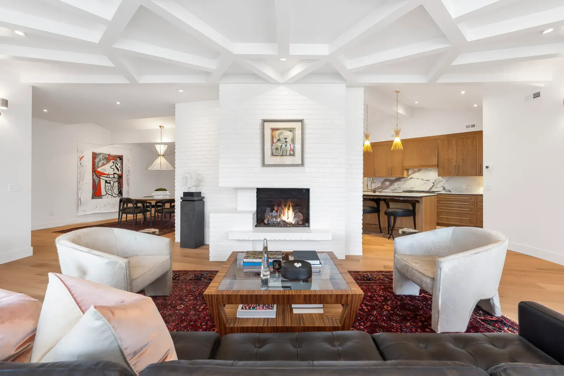 Bright modern living room with white fireplace, red patterned rug, and open dining and kitchen areas