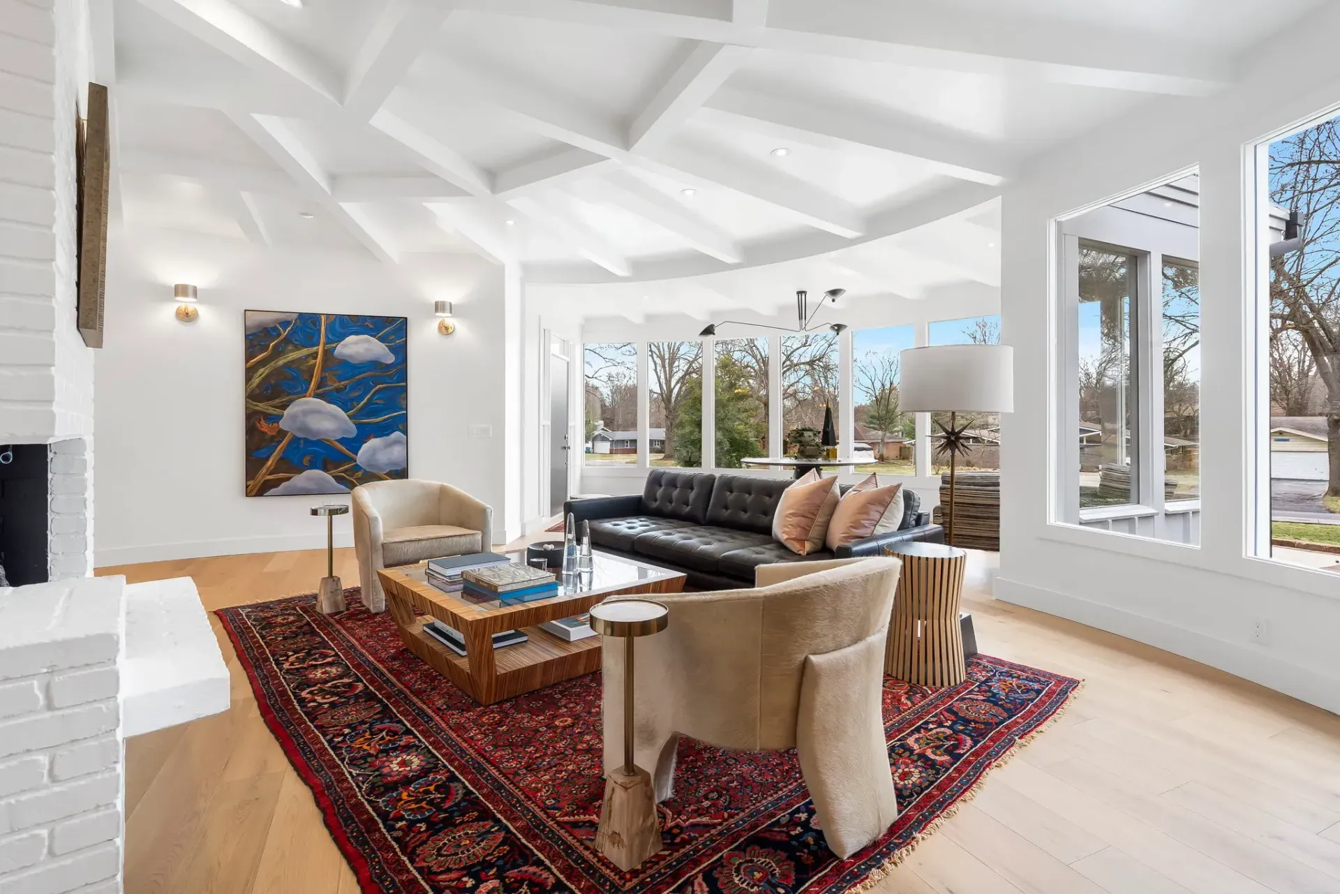 Bright sunroom living space with white ceilings, black sofa, red rug, and large windows.