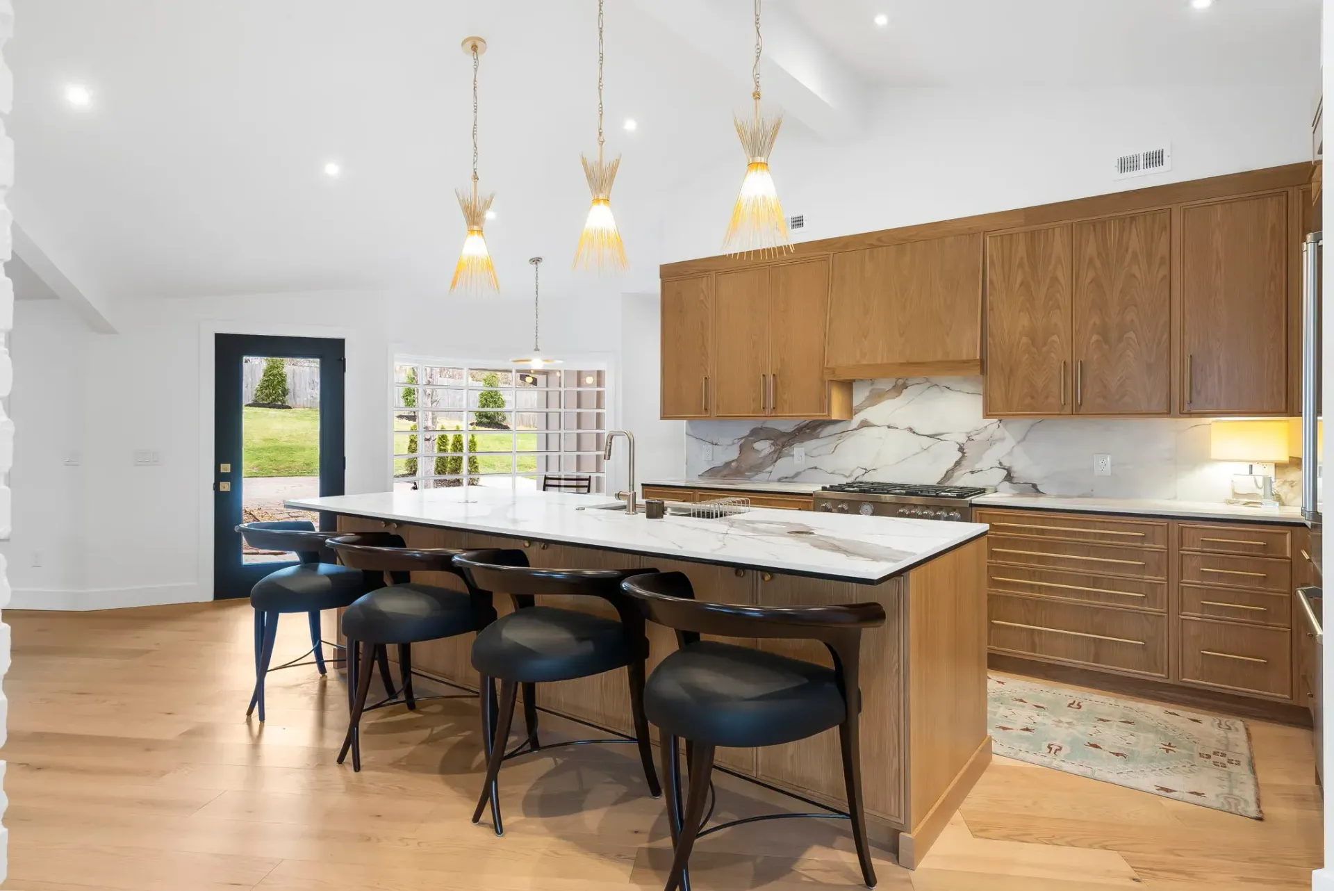 Modern kitchen with island seating, wood cabinets, pendant lights, and large windows