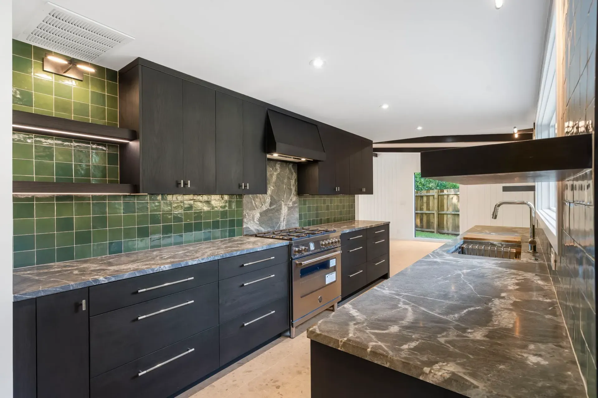 Modern kitchen with dark cabinets, marble countertops, and a long island under bright recessed lights