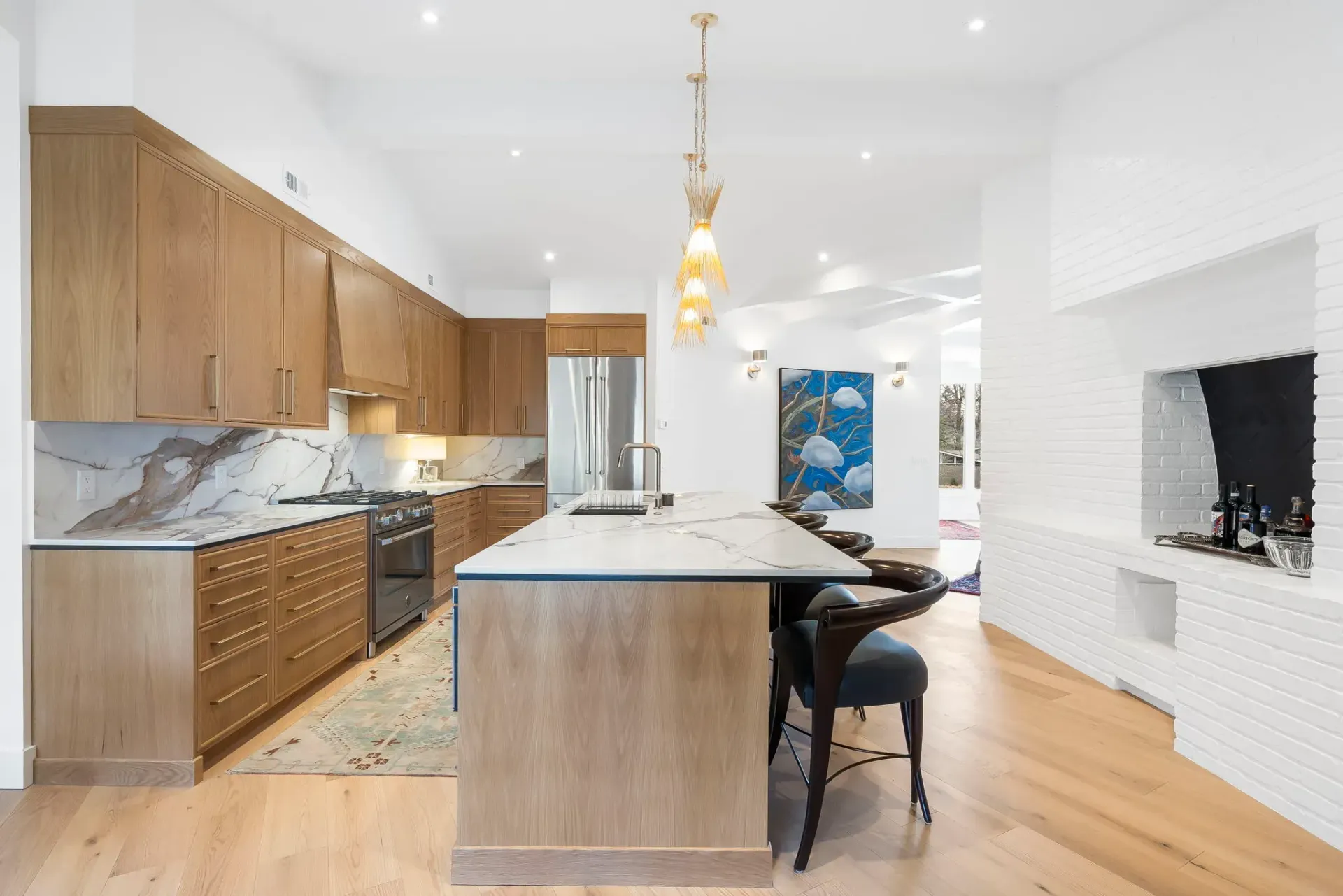 Modern kitchen with wood cabinets, marble island, pendant light, and white fireplace wall