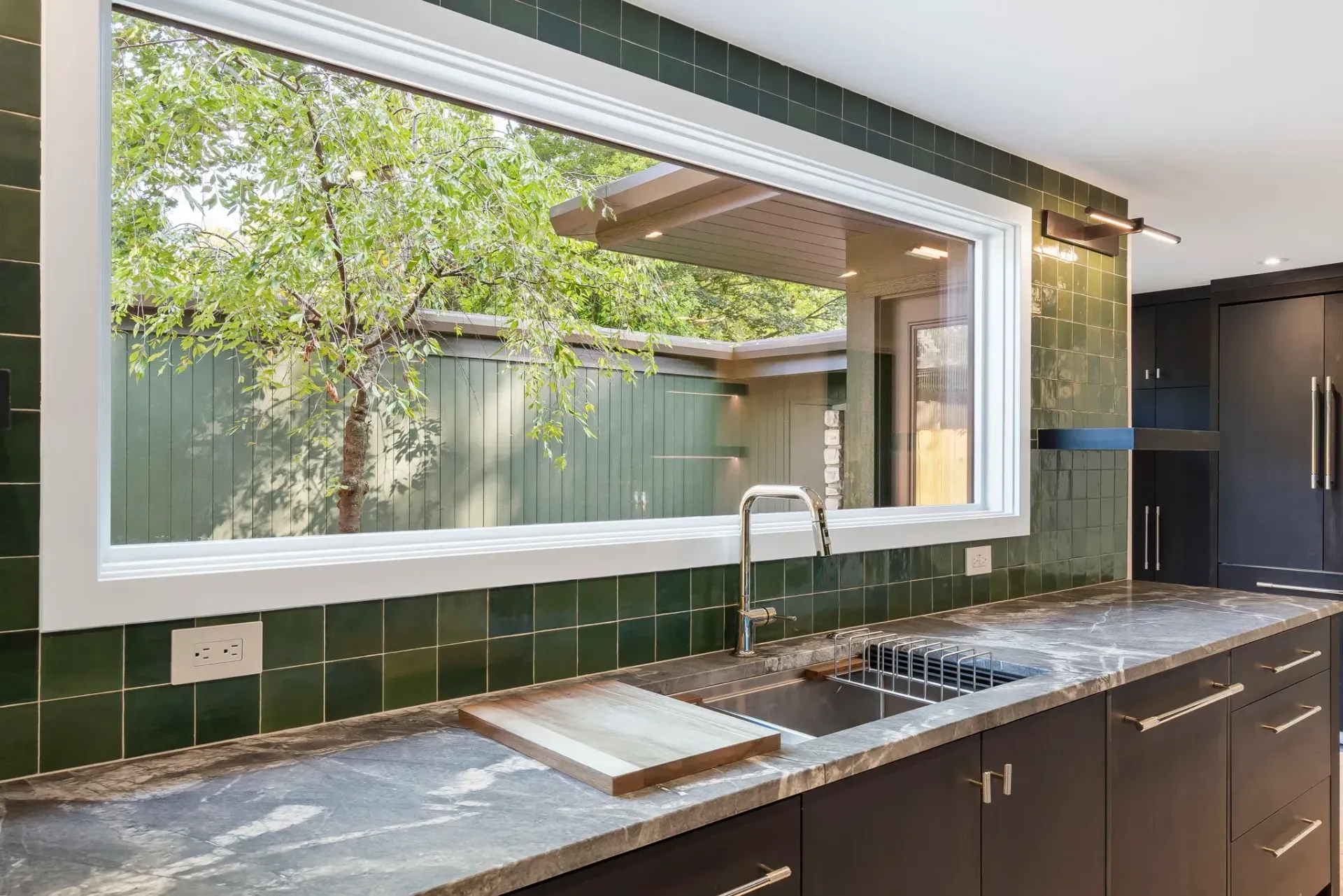 Modern kitchen with green tile backsplash, long window, and stone countertop with sink