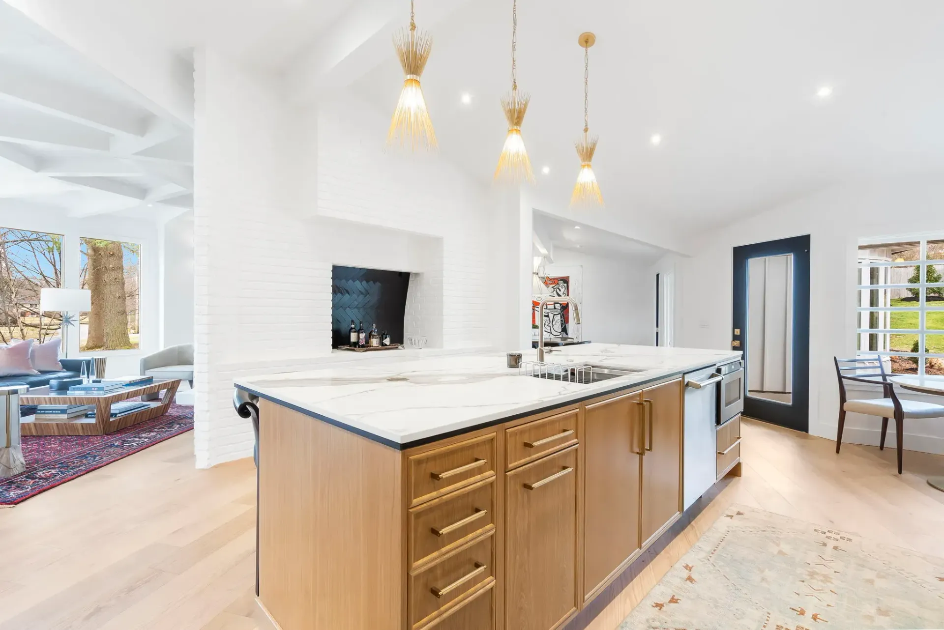 Bright modern kitchen with white cabinetry, large island, and gold pendant lights, opening to a living area