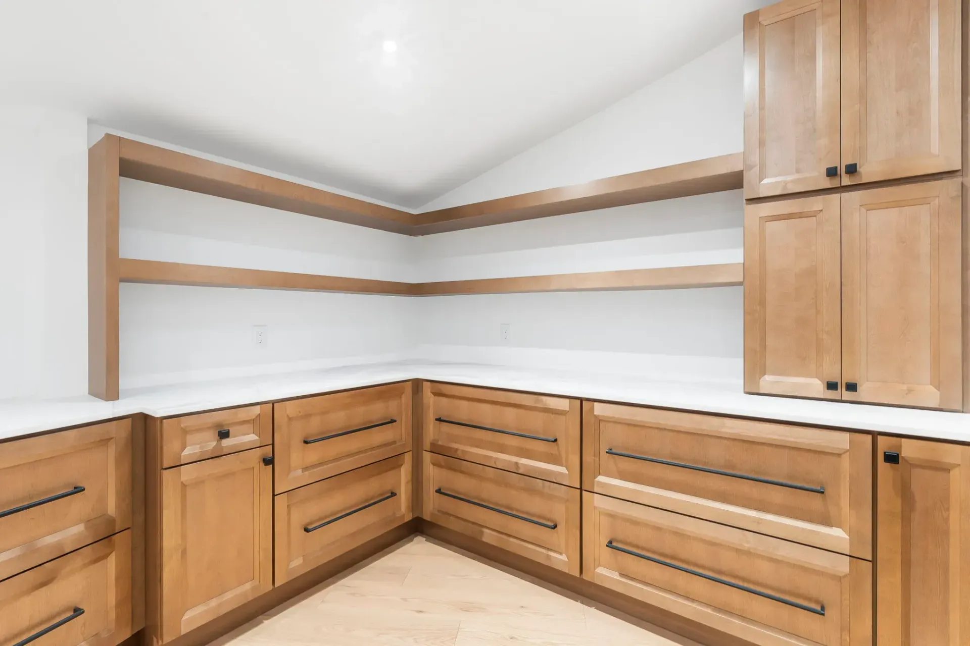 Empty walk-in pantry with wooden cabinets, shelves, and light walls.
