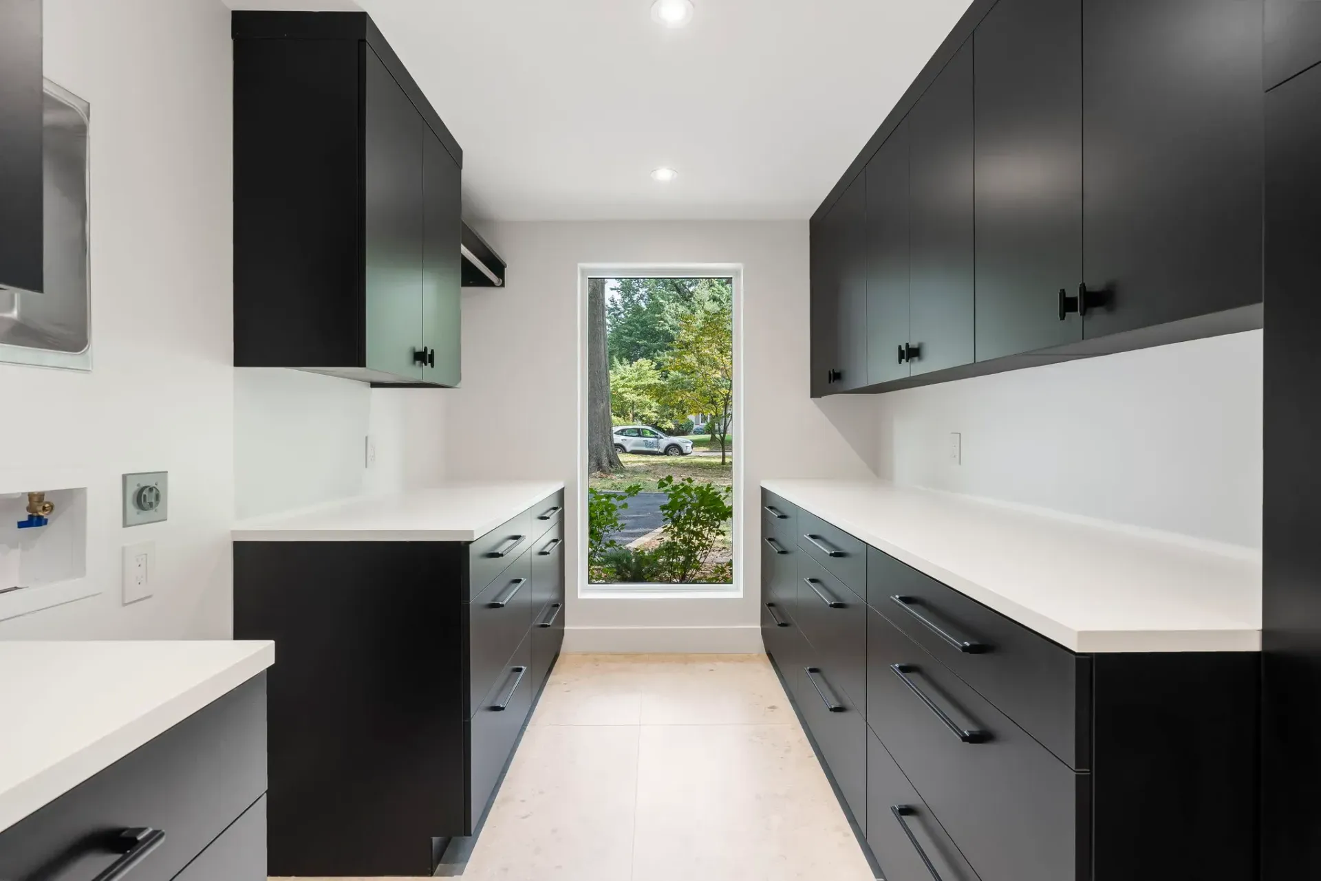Modern galley kitchen with black cabinets, white countertops, and a window at the end