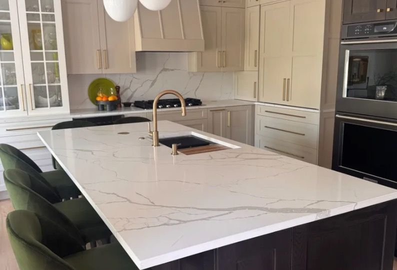 Modern kitchen with white marble island, black cabinetry, brass faucet, and built-in oven