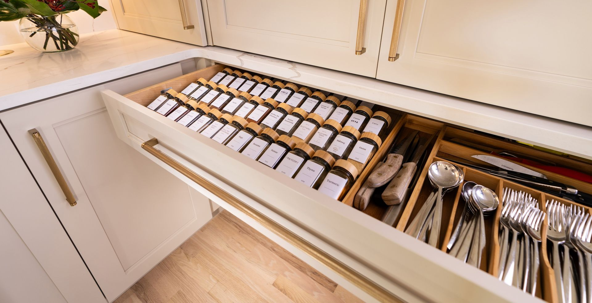 Open kitchen drawer organizer with labeled spice jars and neatly arranged utensils
