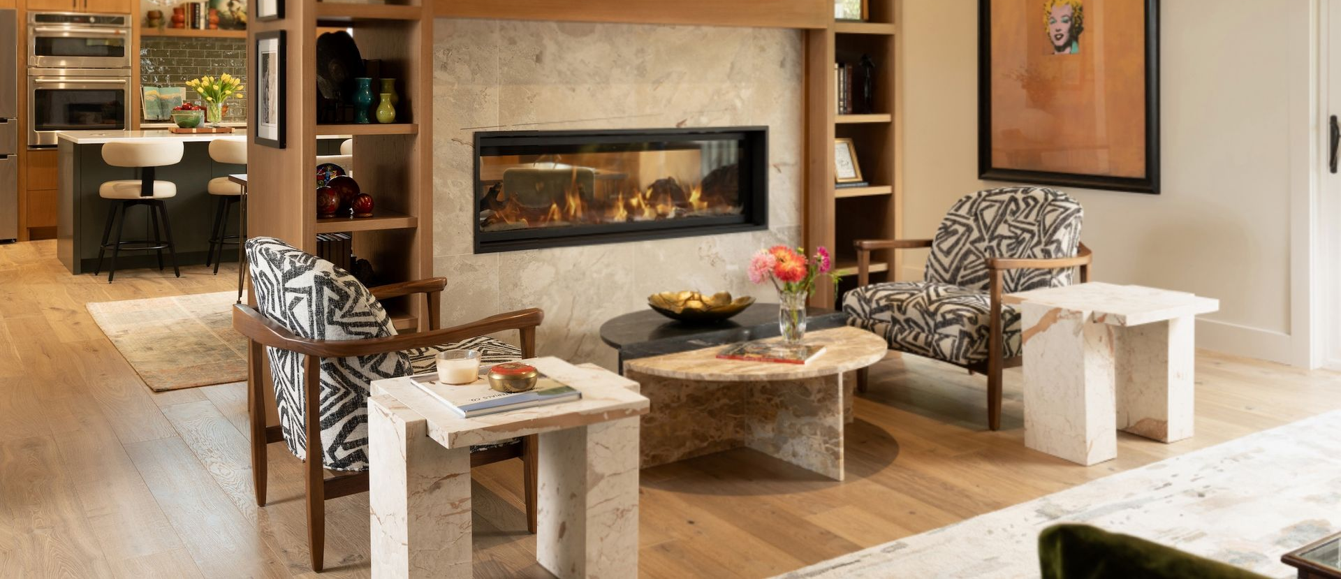 Modern living room with a fireplace, patterned chairs, and white side tables on a light wood floor