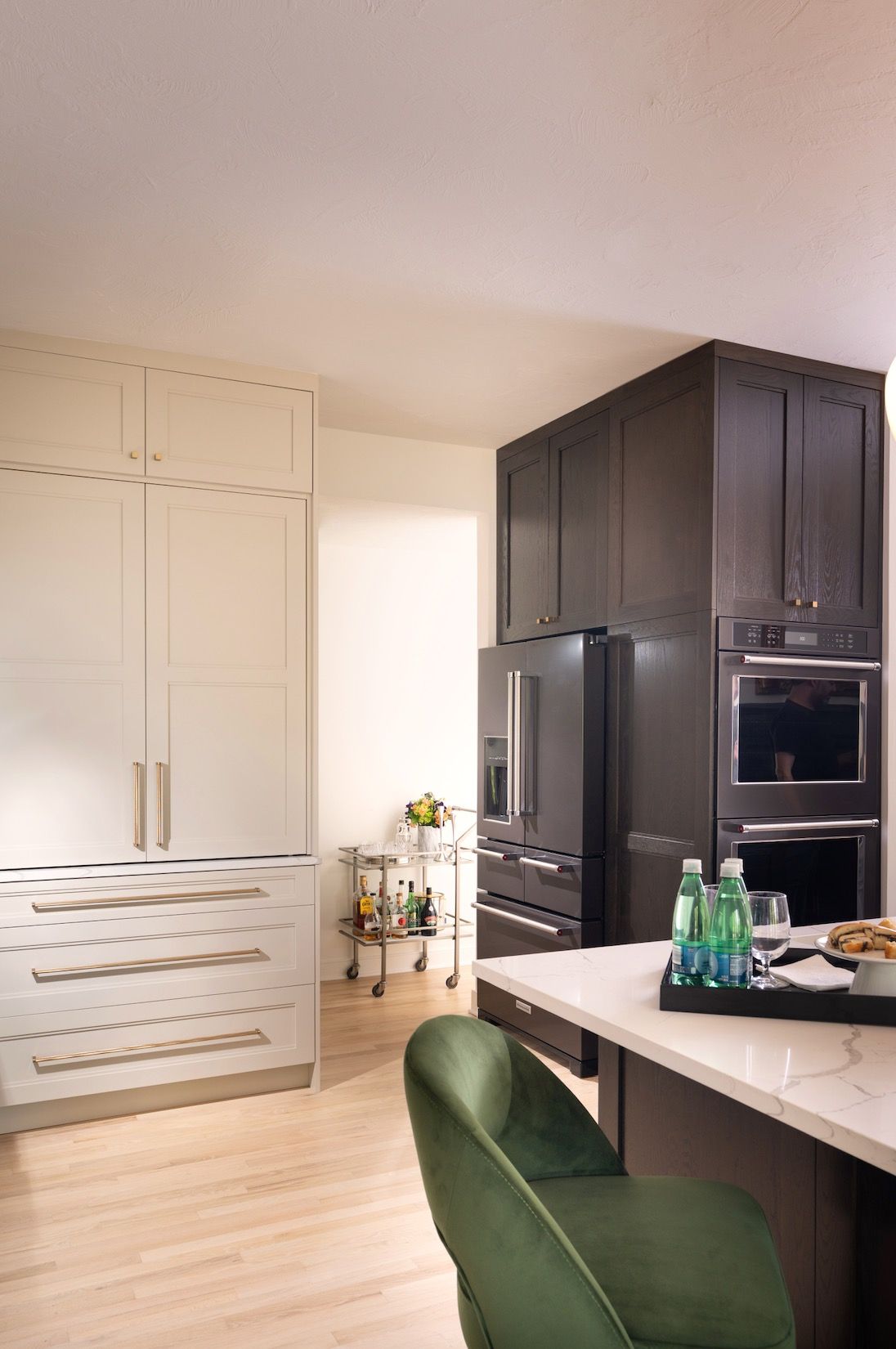 Modern kitchen with black cabinets, white island, and green barstool near a bright entryway