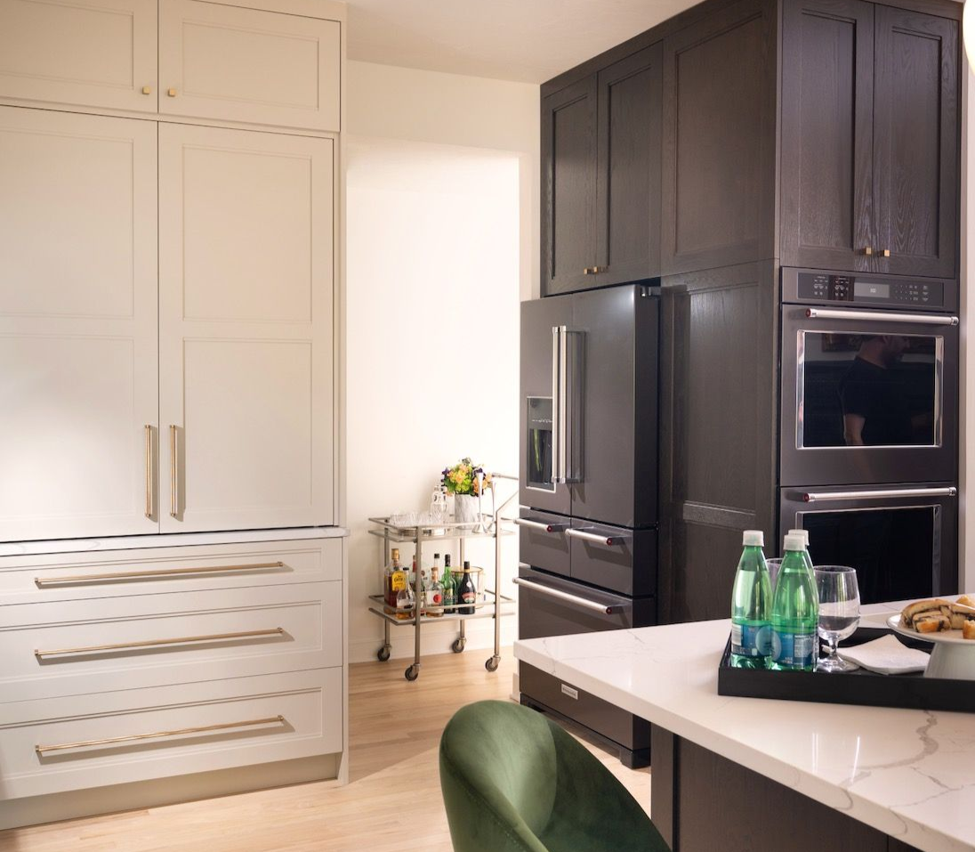 Modern kitchen with white cabinets, dark refrigerator wall, and a white island with green chairs.