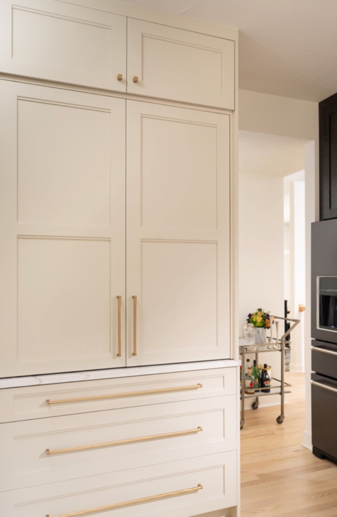 White built-in kitchen cabinets with gold handles in a bright modern interior.