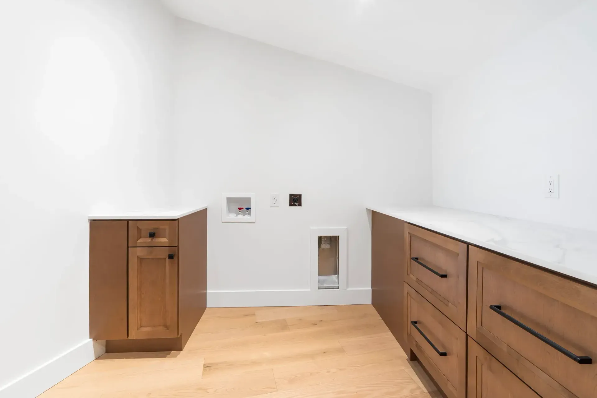Empty white utility room with light wood cabinets, countertop, and pet-access openings in the wall