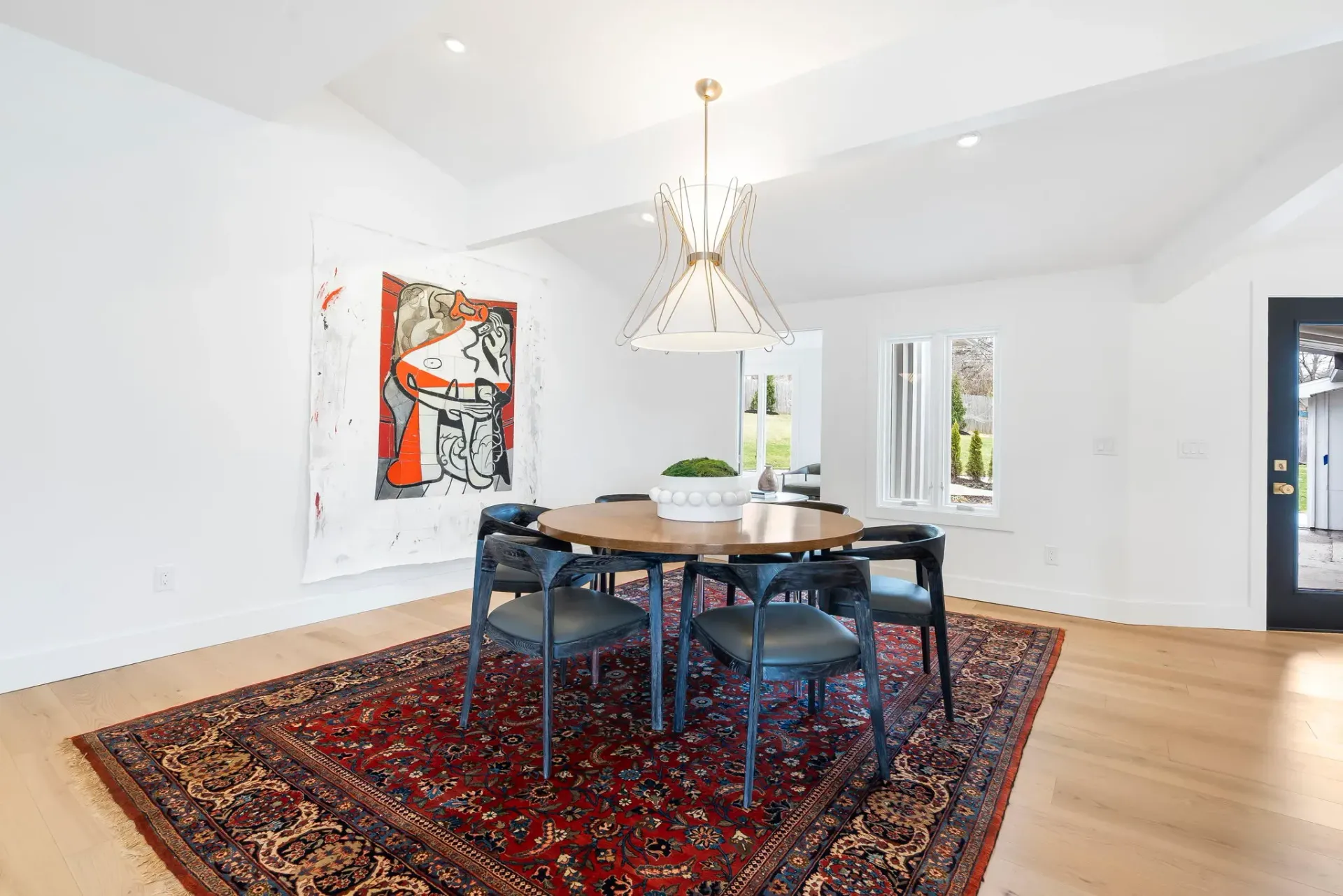 Modern dining room with black chairs, a wooden table, red rug, and colorful wall art
