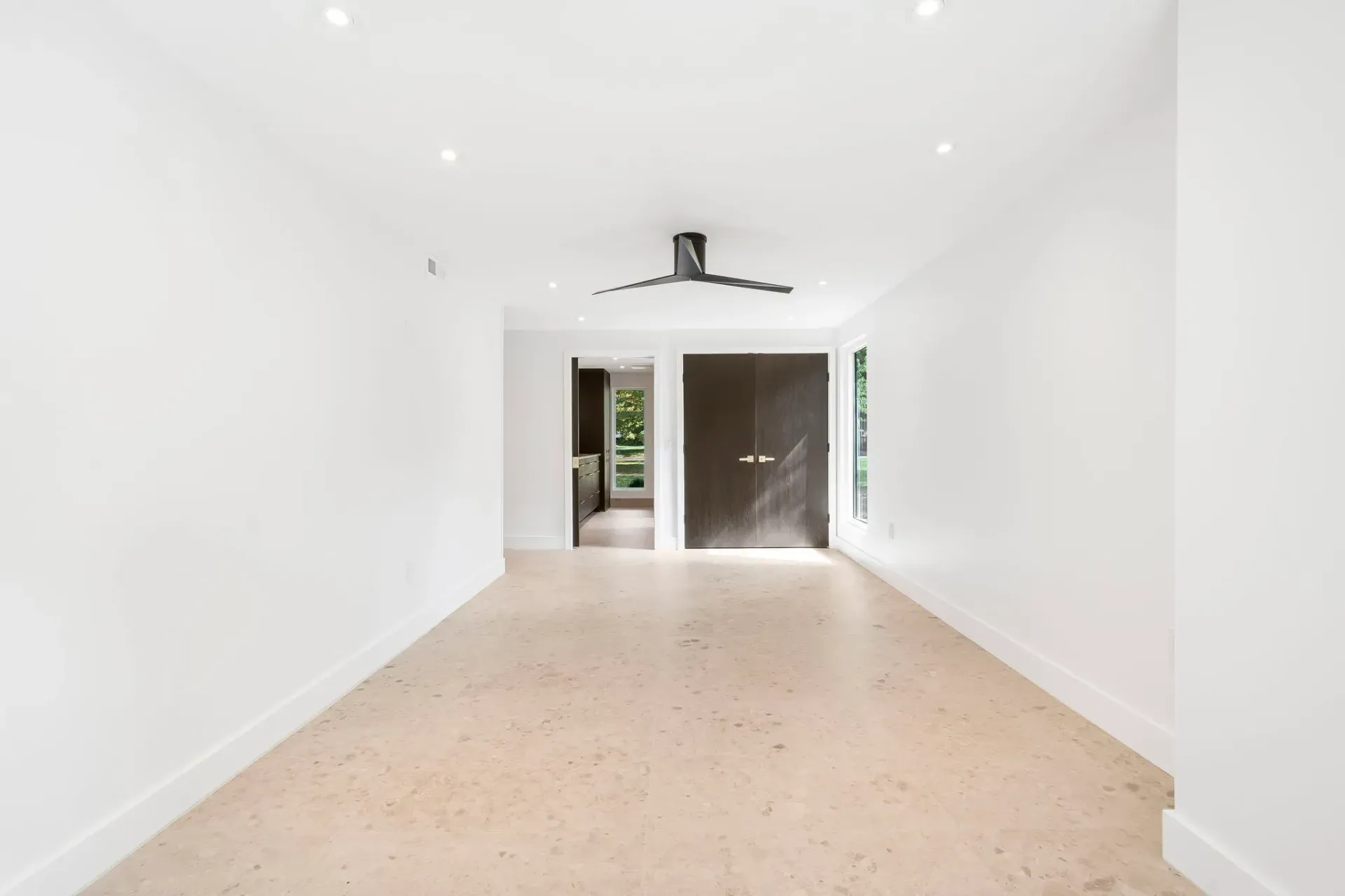 Empty white room with beige speckled floor and double doors at the far end.