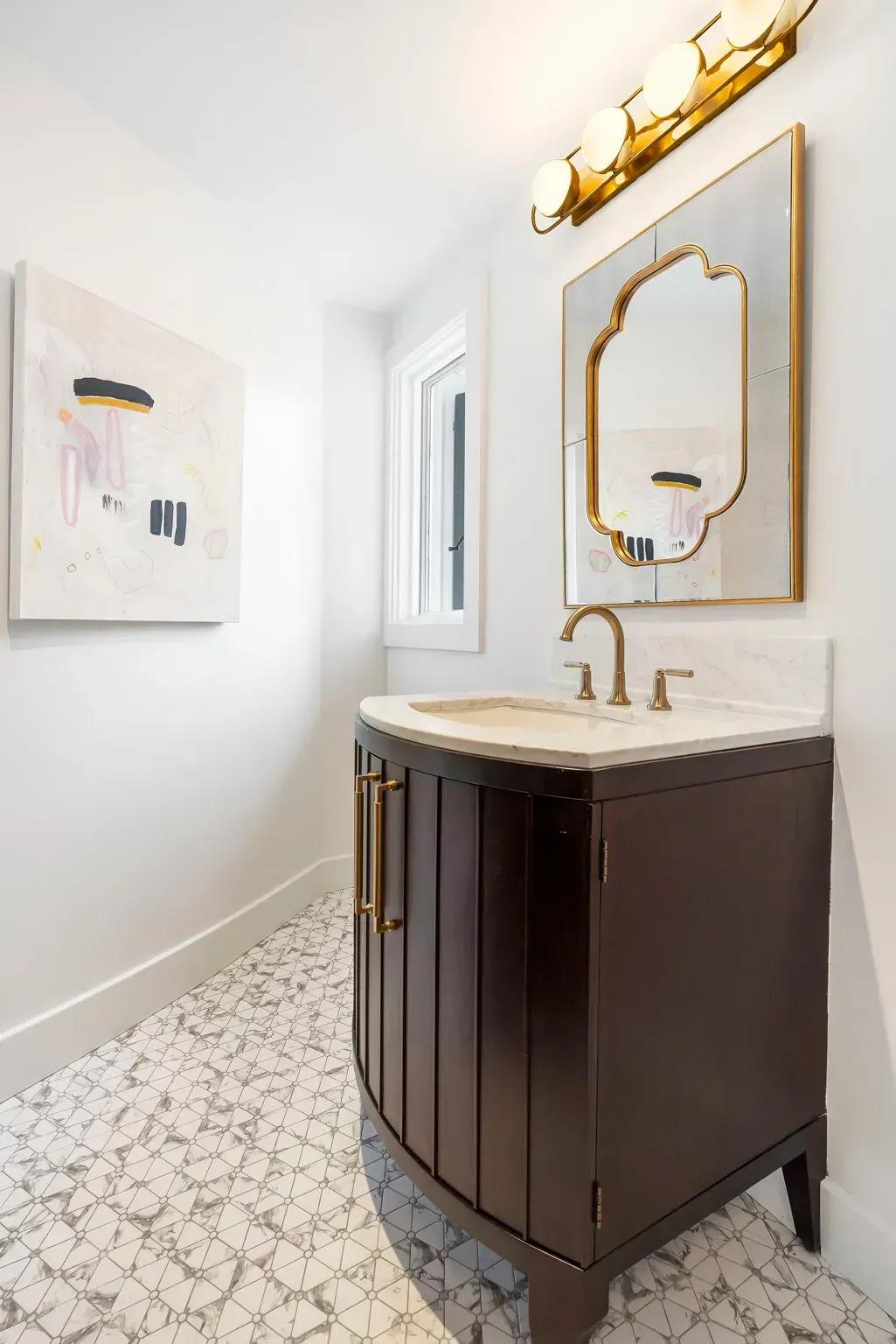 Modern bathroom vanity with dark wood cabinet, gold mirror, white sink, and patterned tile floor.