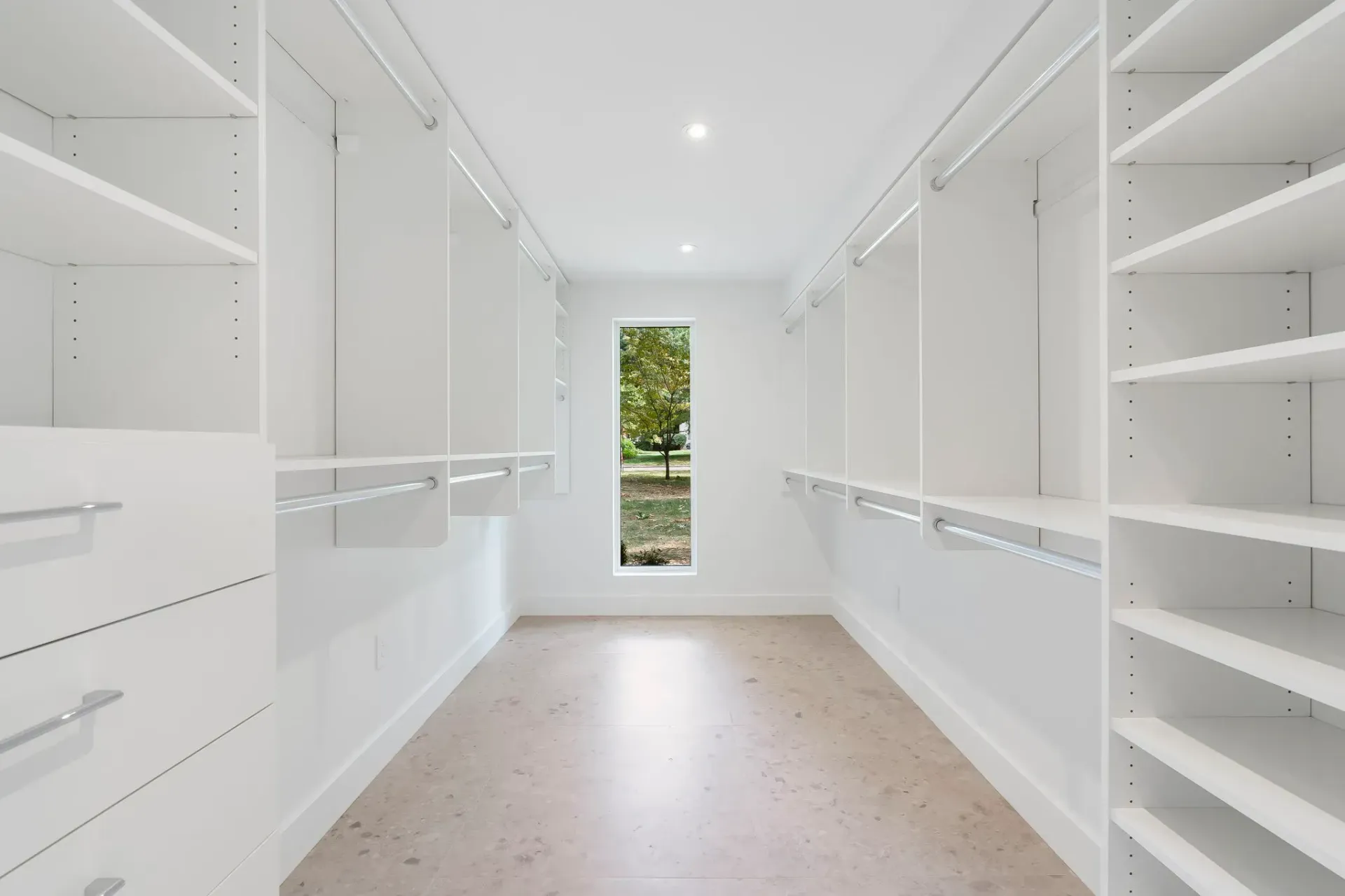 Bright white walk-in closet with built-in shelves, hanging rods, and a narrow window at the far end