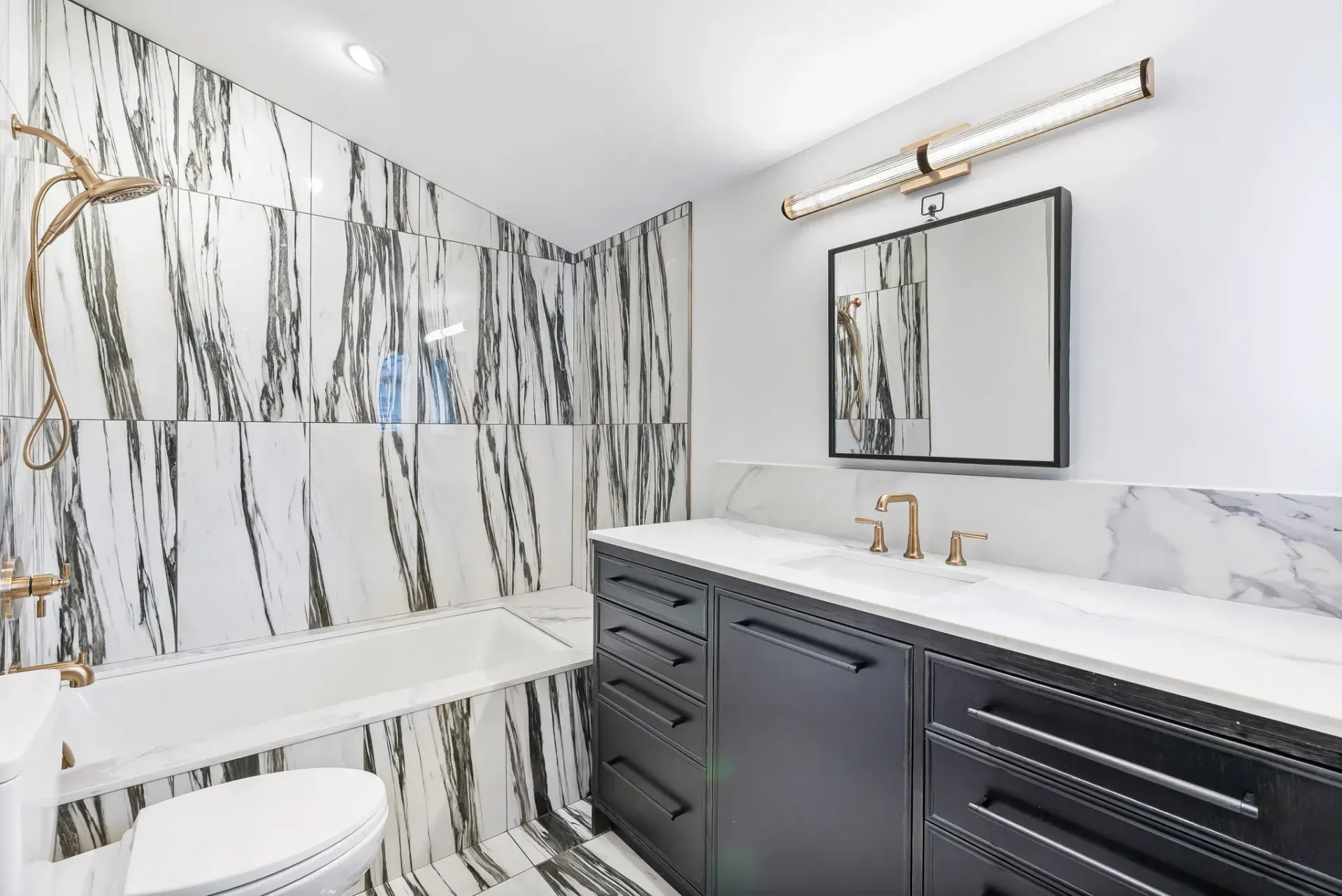 Modern bathroom with black-and-white marble walls, dark vanity, mirror, and a bathtub.