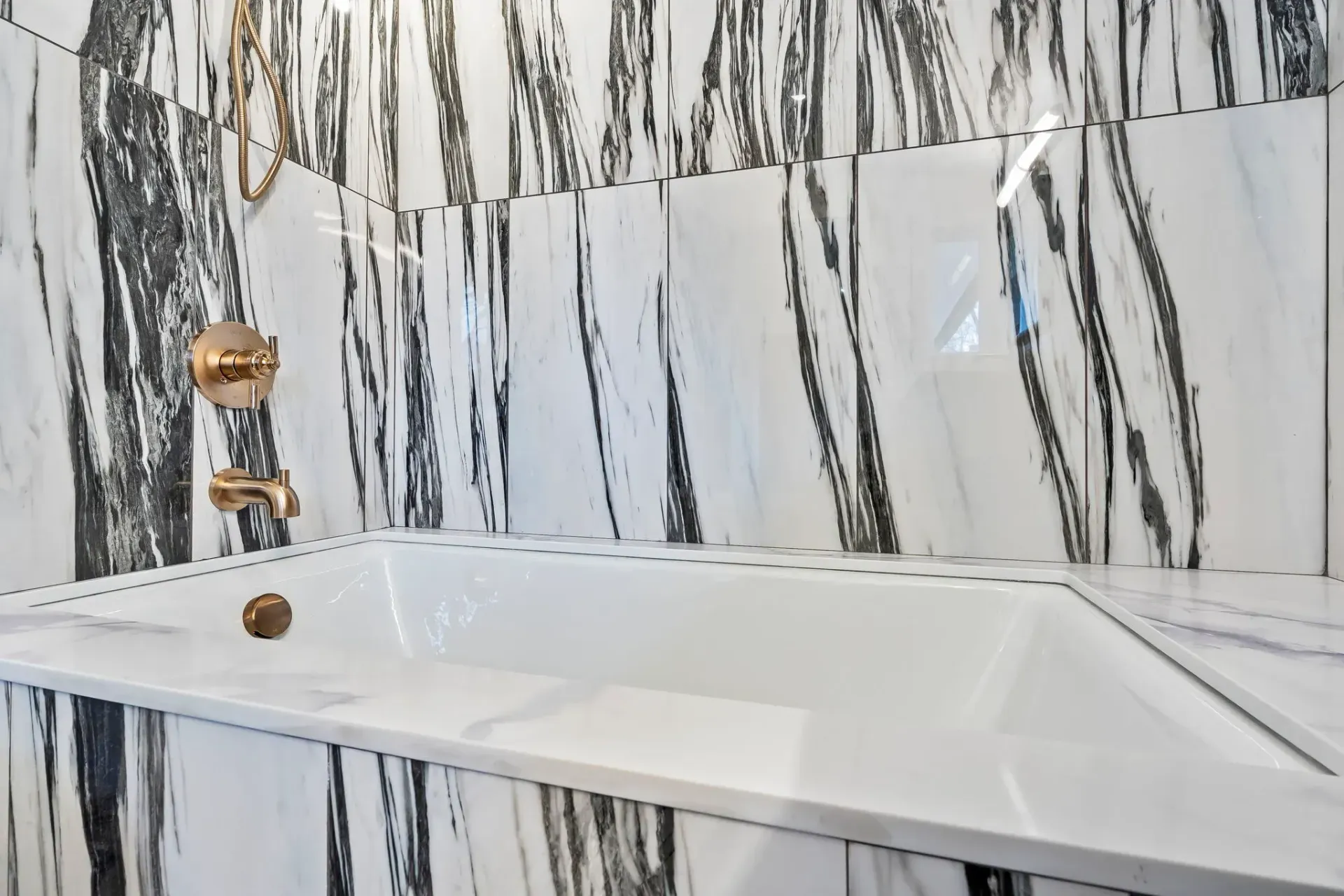 Modern white bathroom sink with marble-patterned wall and gold faucet