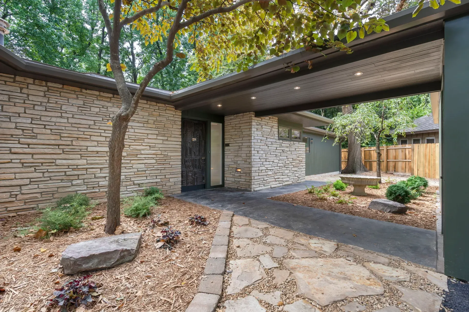 Modern home entrance with stone walkway, brick walls, and a tree-shaded courtyard