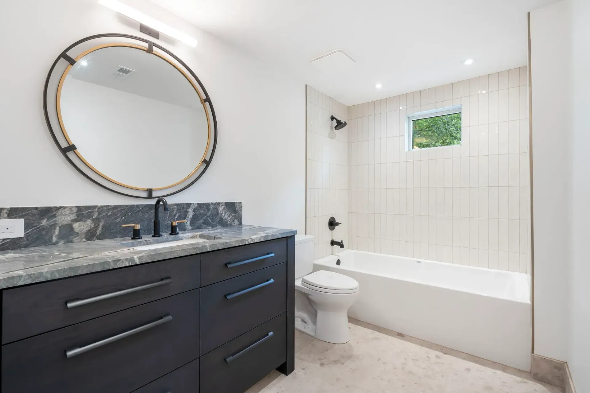 Modern bathroom with dark vanity, round mirror, and white tub shower area