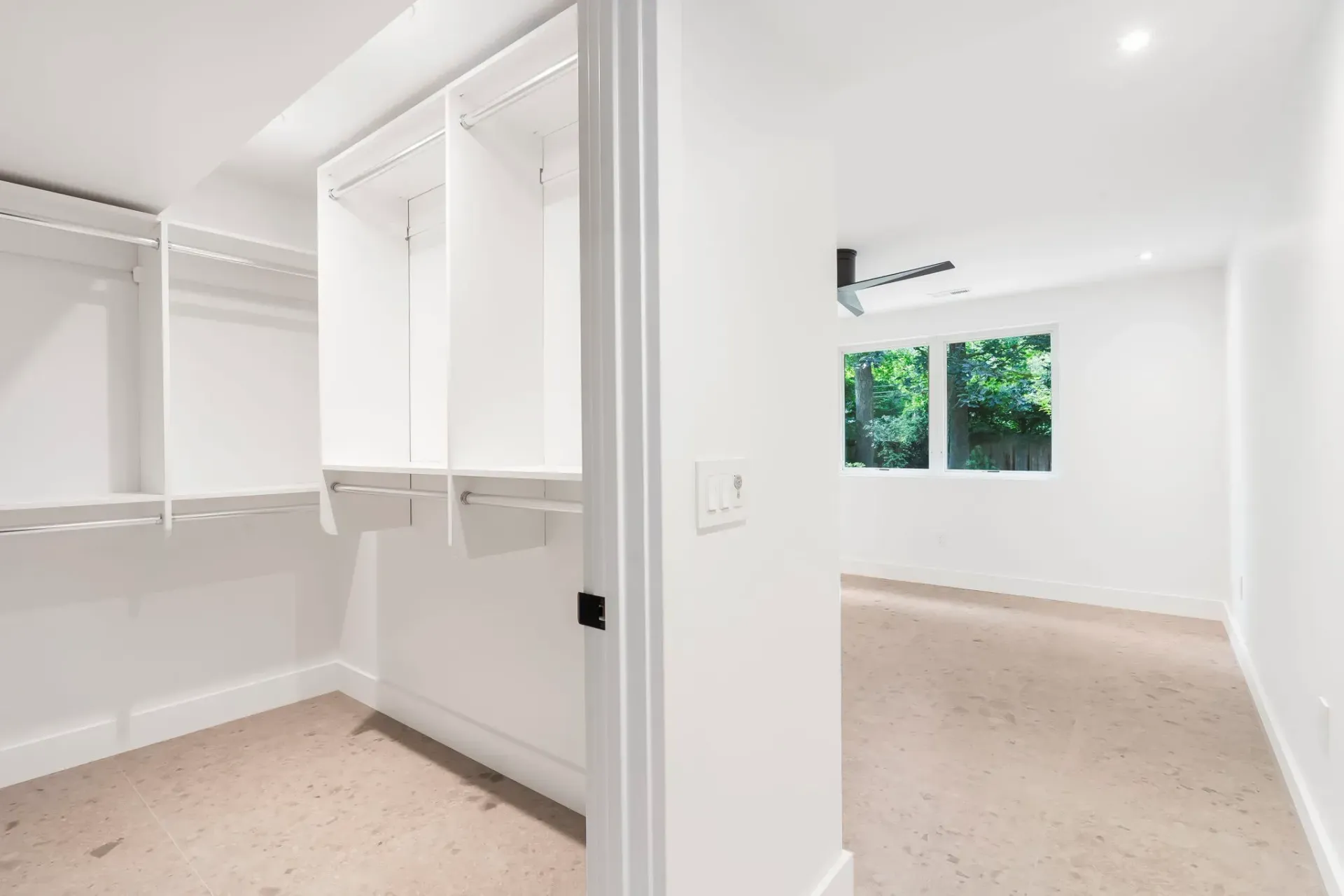 Empty bright room with white walls, built-in closet, and two windows overlooking greenery