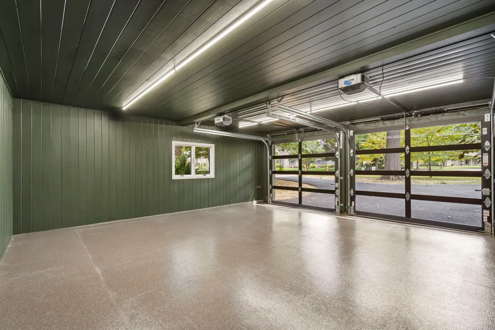 Empty green garage interior with polished floor, LED ceiling lights, and glass doors opening to greenery