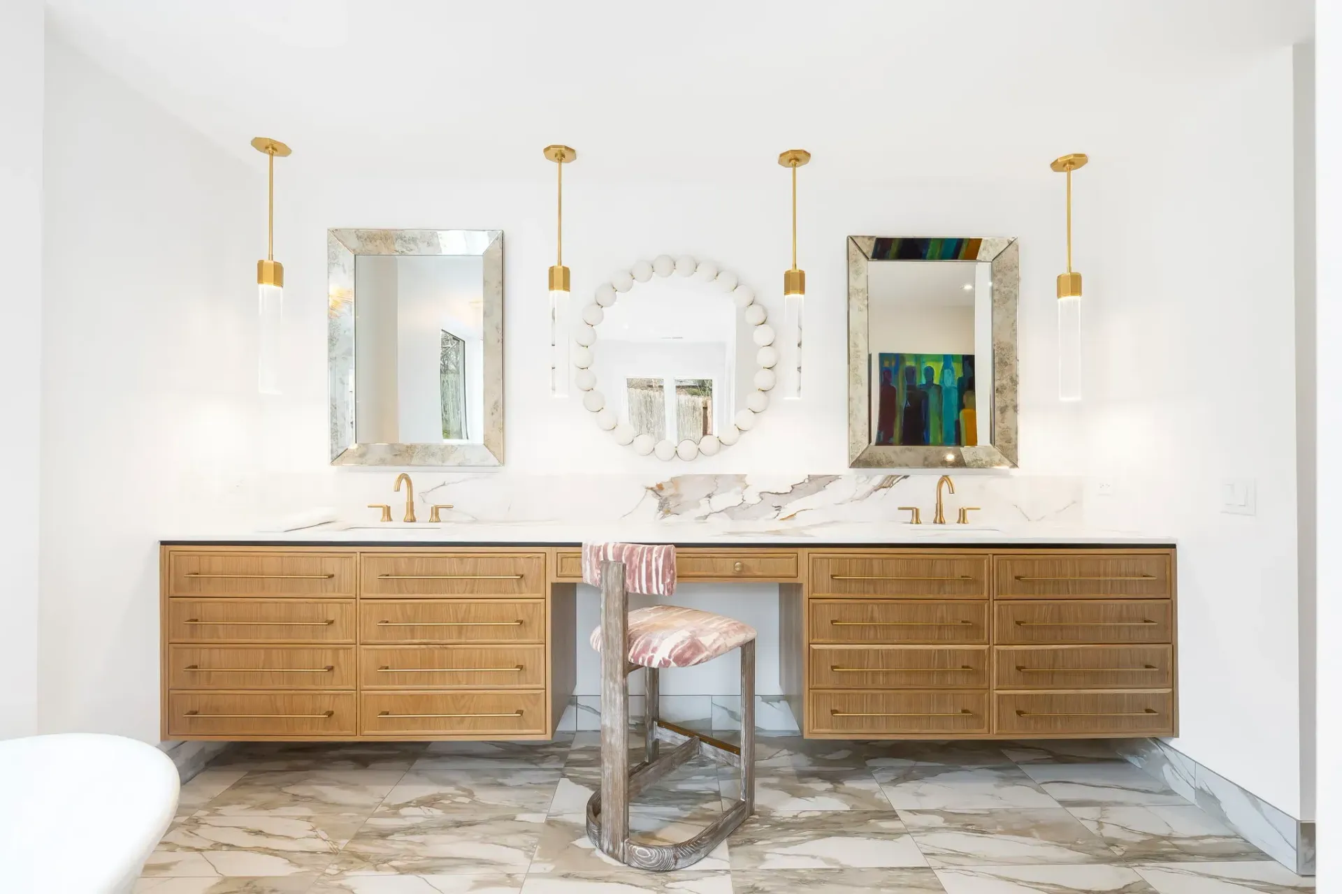 Bright vanity room with two wooden cabinets, three mirrors, gold sconces, and a patterned marble floor.