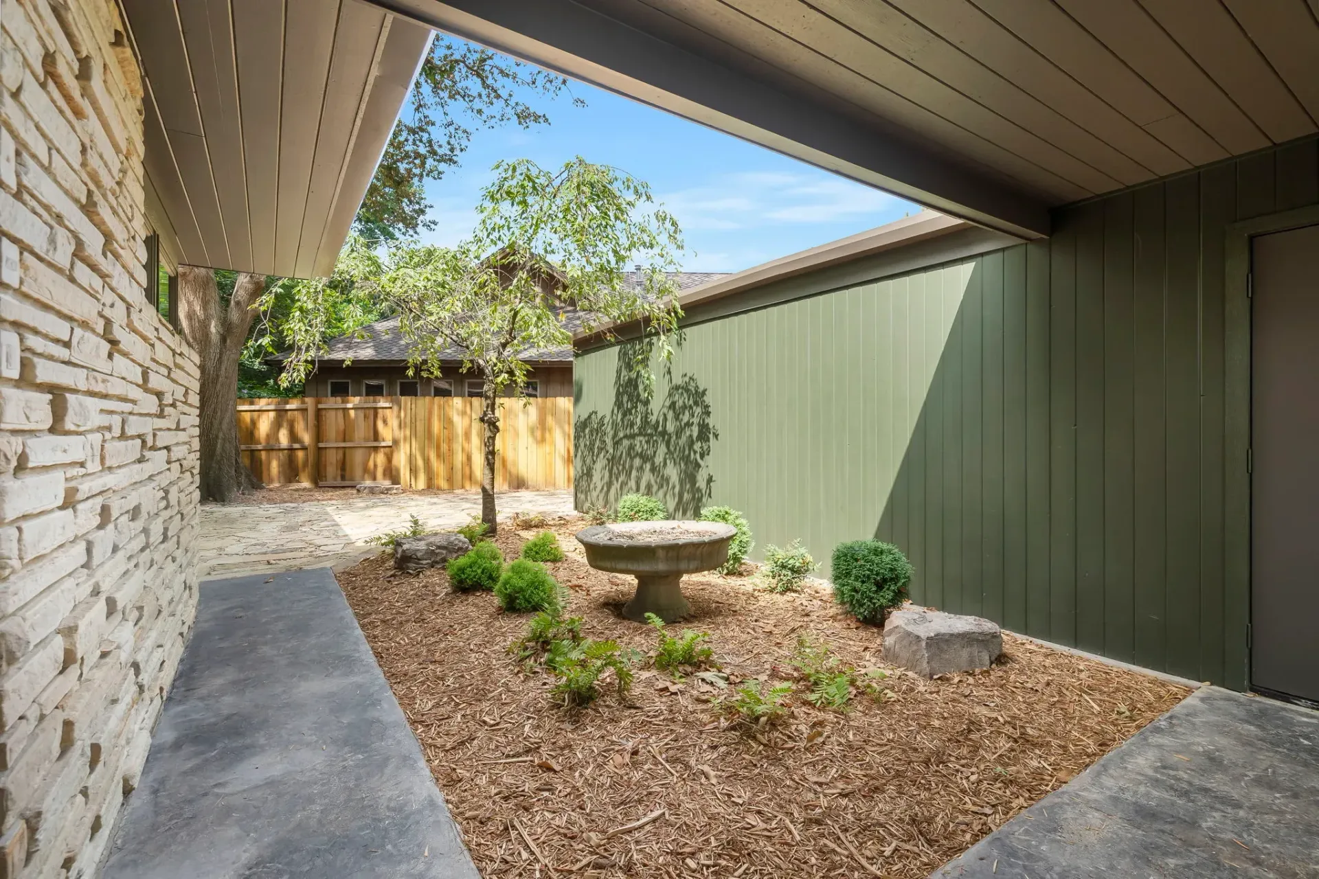Modern backyard courtyard with gravel, a raised planter, and stone and green walls under a covered patio