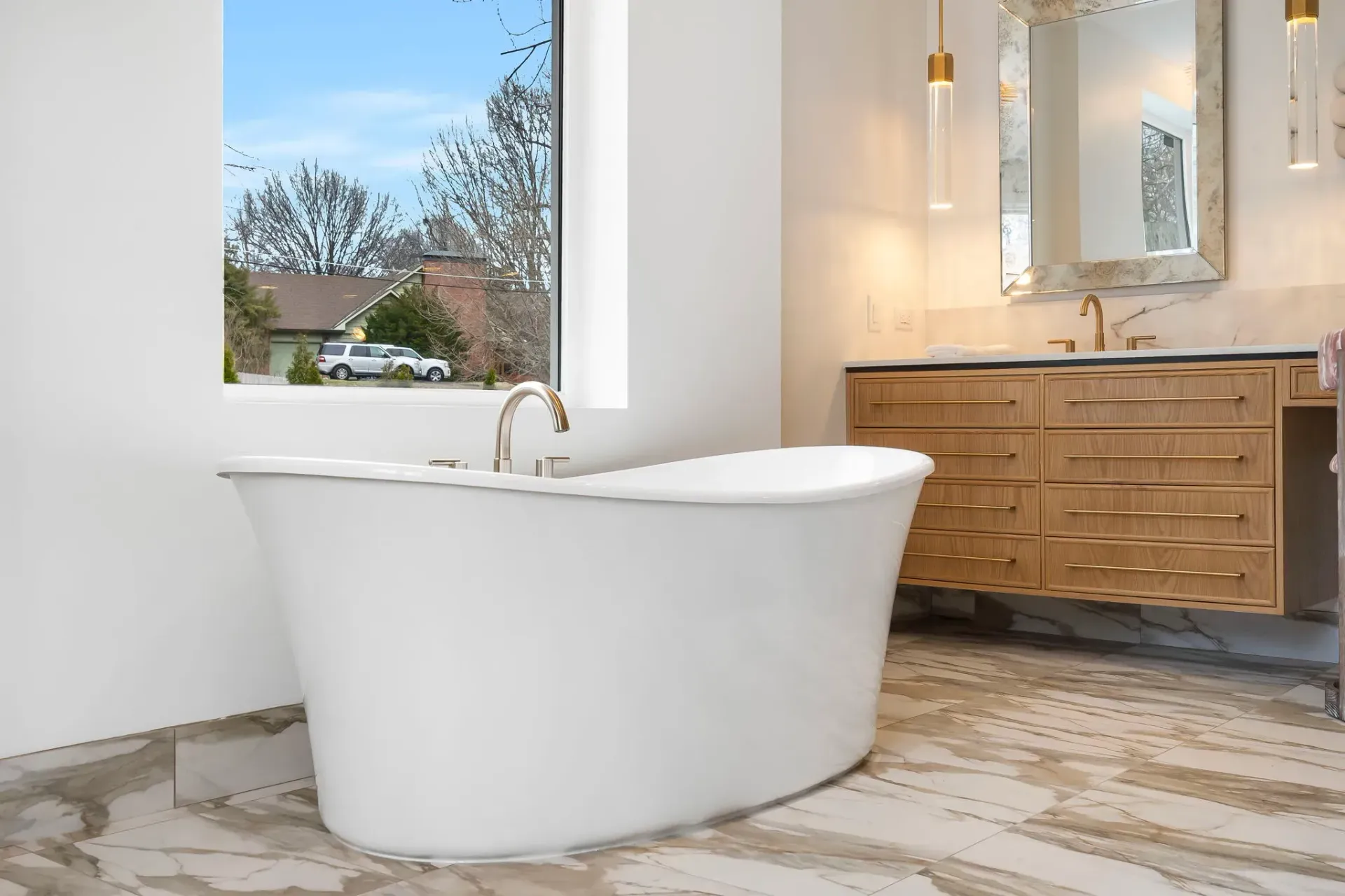 Modern bathroom with a white freestanding tub, wood vanity, and large window with a scenic view