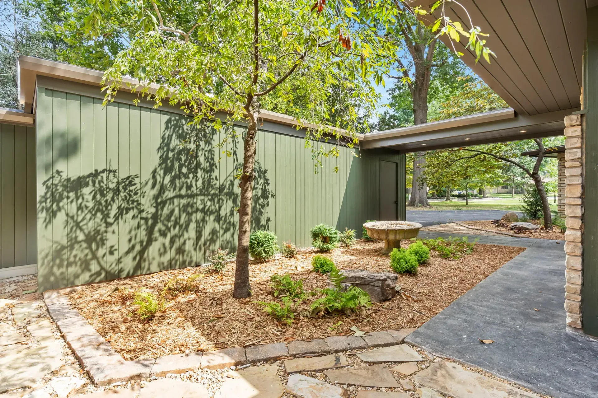 Backyard patio with trees, gravel paths, and a green fence beside a covered deck
