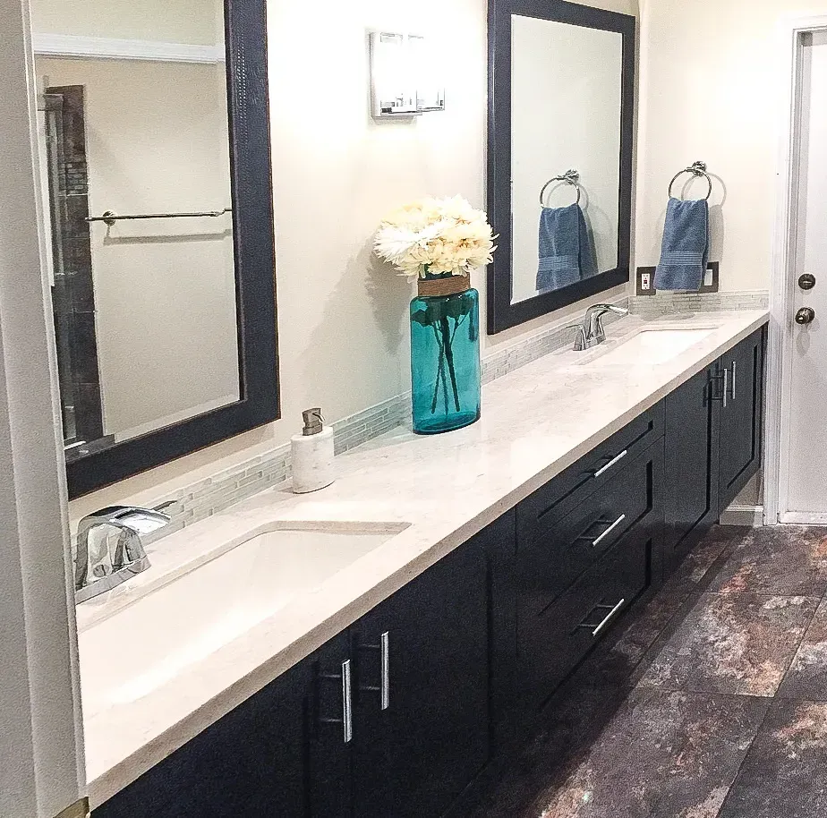 Modern bathroom vanity with double sinks, black cabinets, large mirror, and teal vase with flowers.