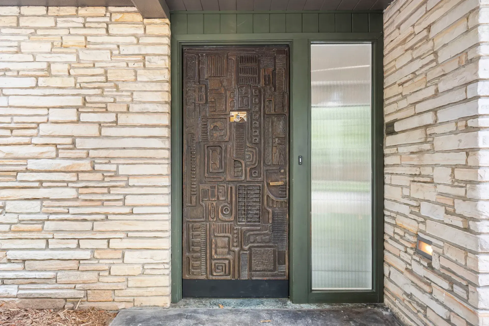 Front door with dark carved wood and frosted glass sidelight in a brick exterior wall