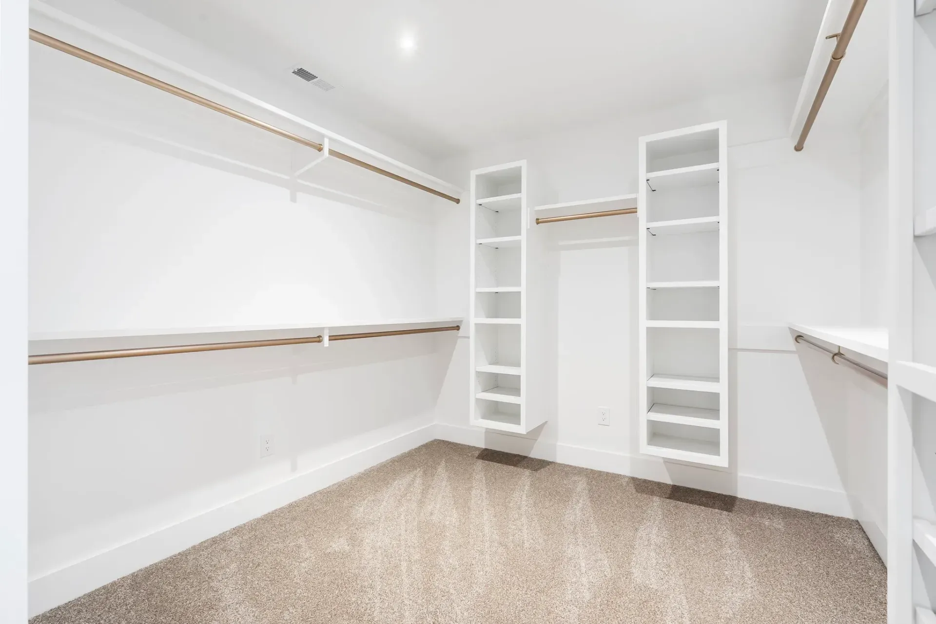 Bright empty walk-in closet with white shelves, hanging rods, and carpeted floor.