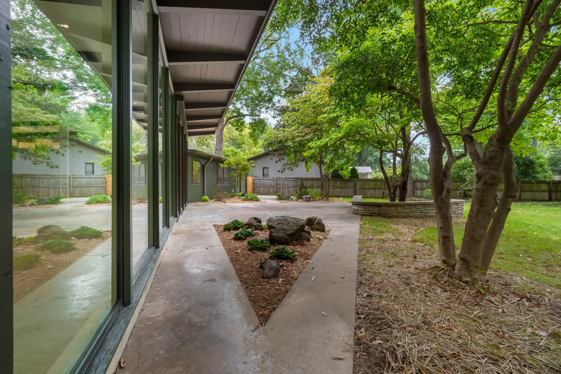 Modern courtyard walkway beside glass windows, concrete planters, and trees under a covered roof