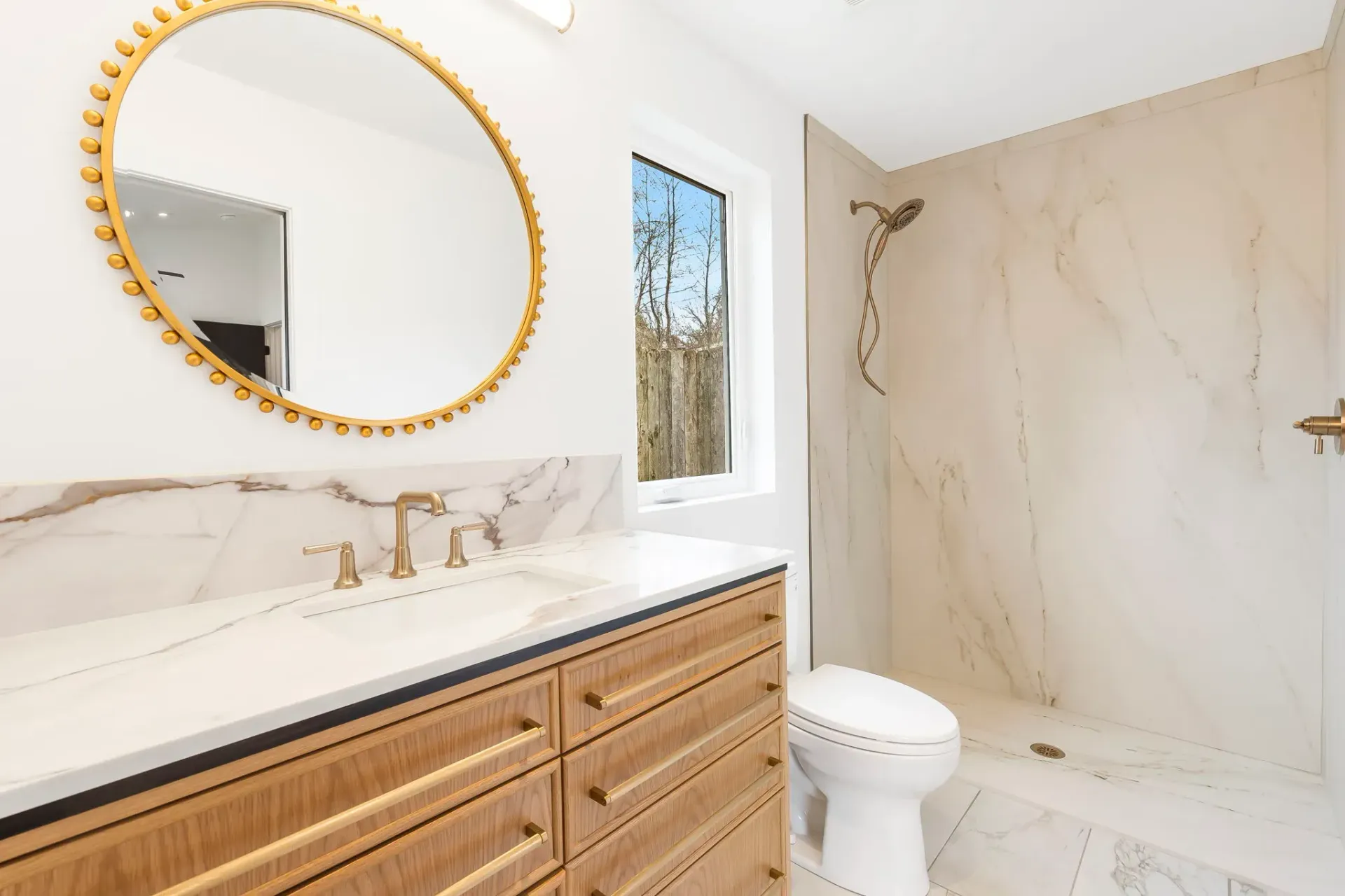 Modern bathroom with gold-framed mirror, marble vanity, and glass shower.