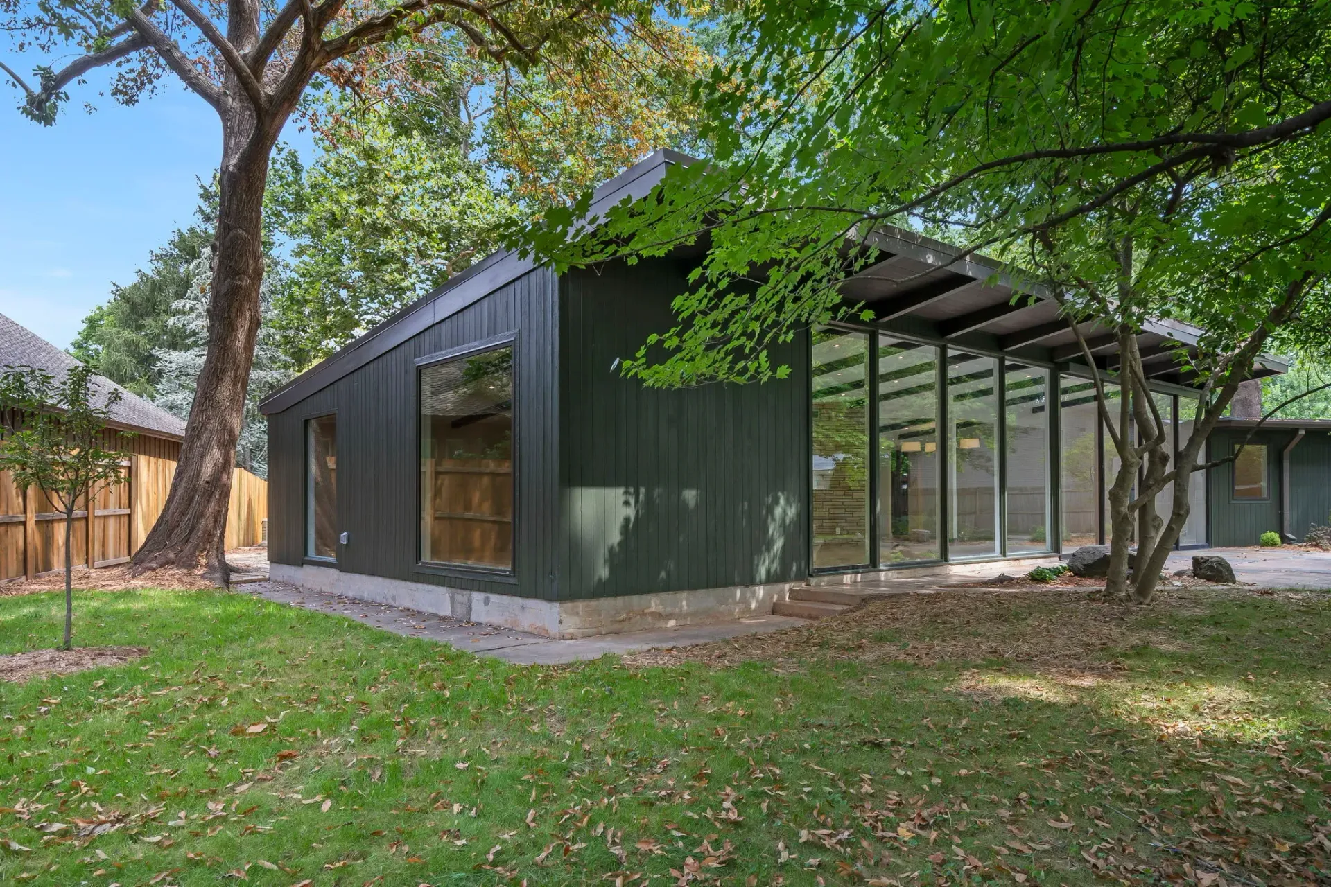Modern dark-green house with large glass walls amid trees and grass