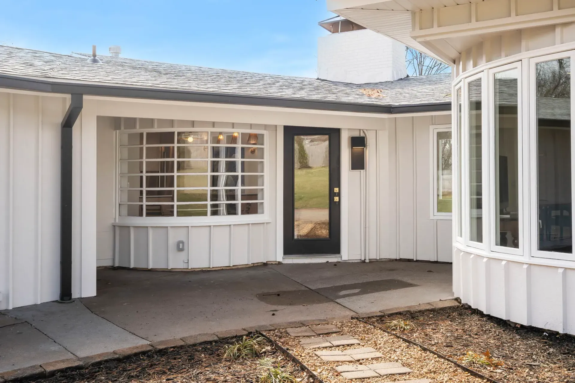 White house entrance with bay window, front door, and covered porch under a tiled roof