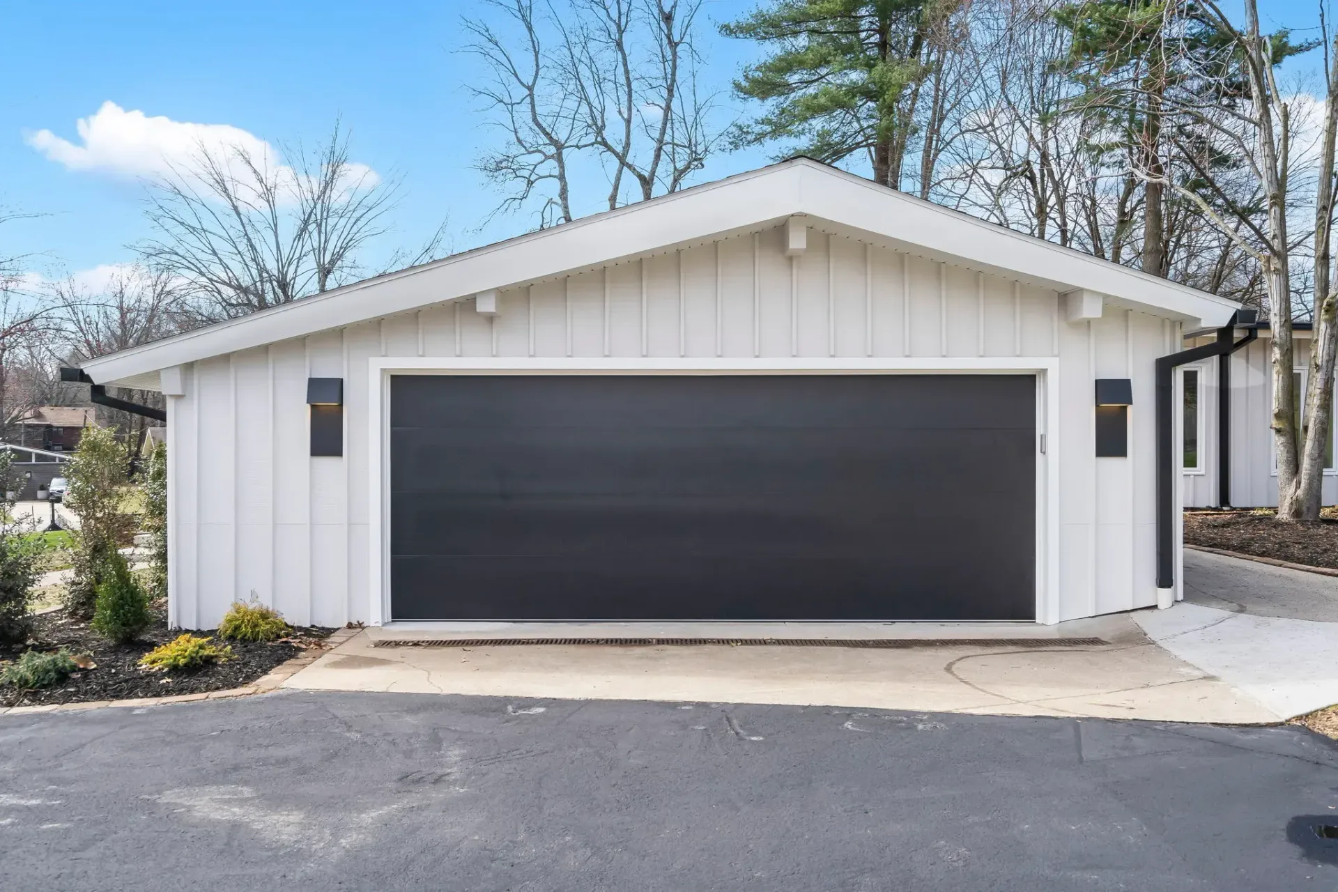 White detached garage with a dark double door and paved driveway under a blue sky