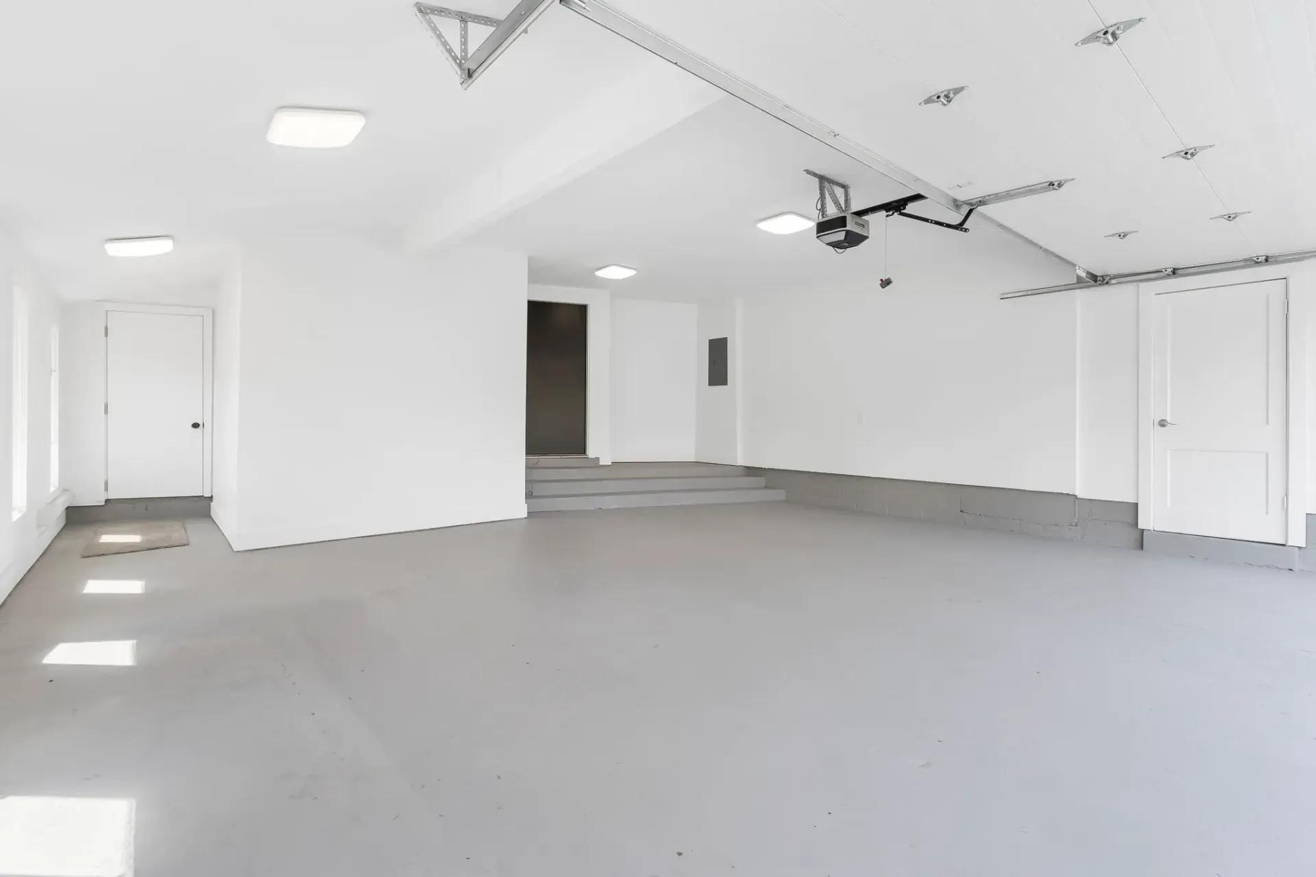 Empty white garage interior with gray floor, overhead lights, and closed doors