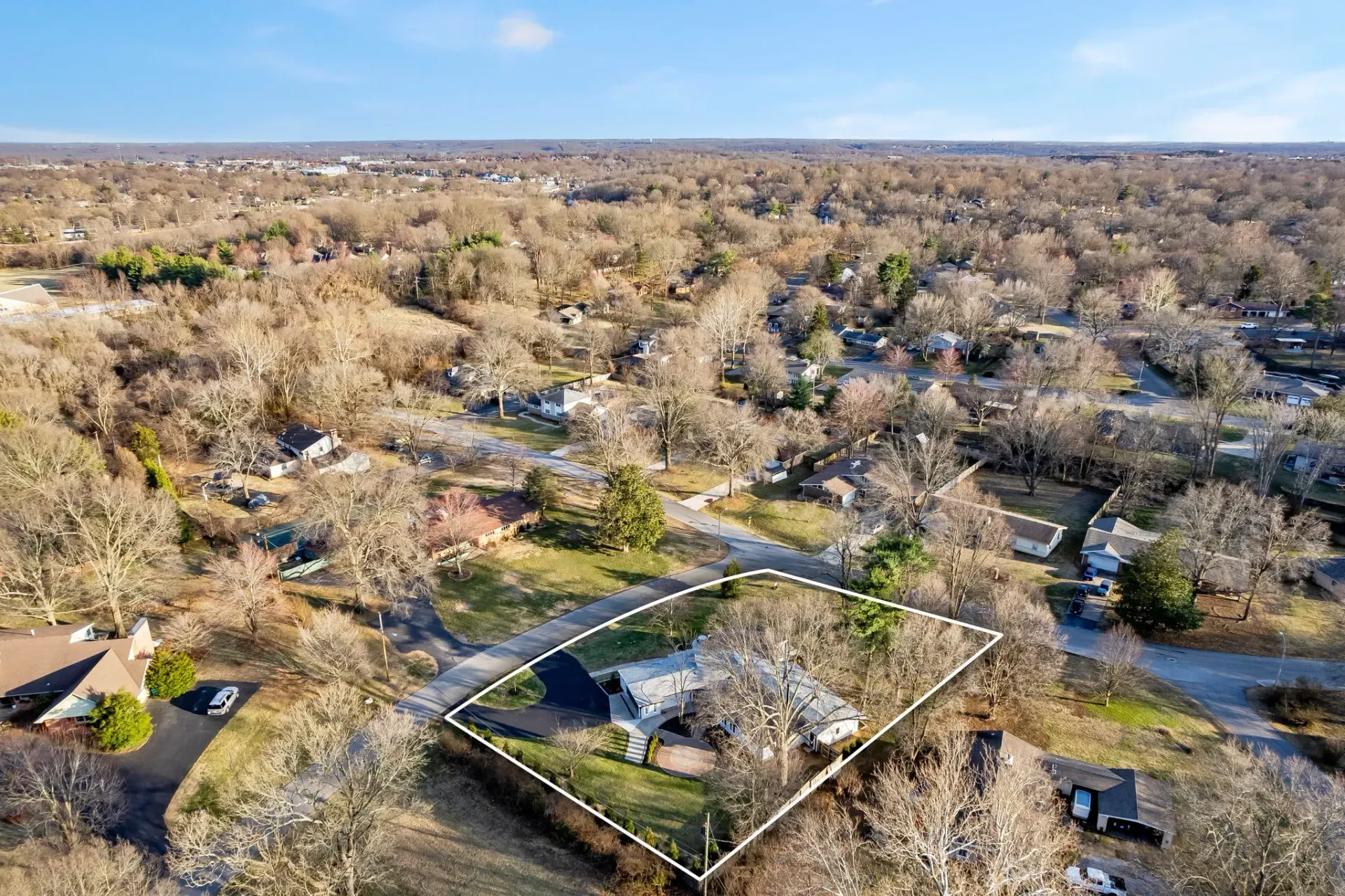 Aerial view of a rural neighborhood with houses, roads, and leafless trees under a clear sky