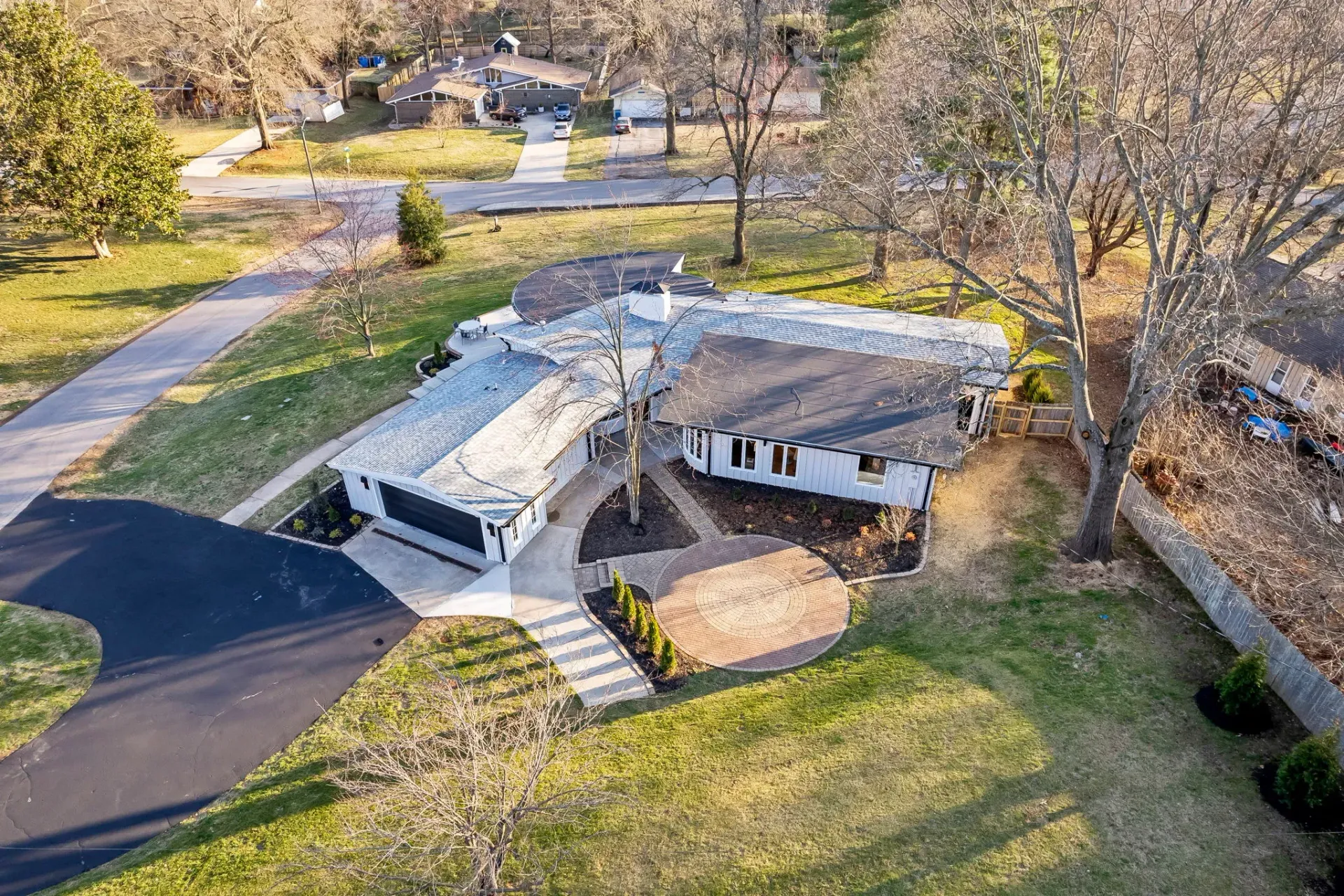 Aerial view of a house with a large damaged roof, surrounded by grass and trees.