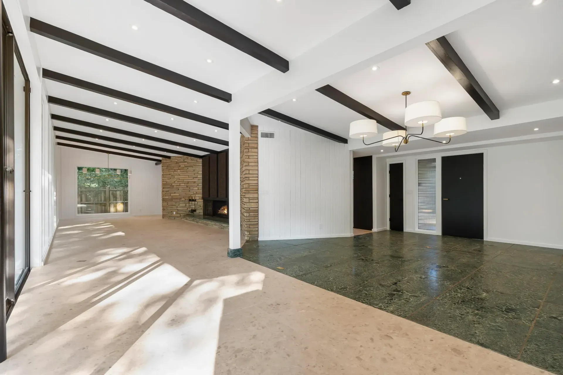 Bright empty living and dining room with exposed beams, white walls, and a dark stone floor